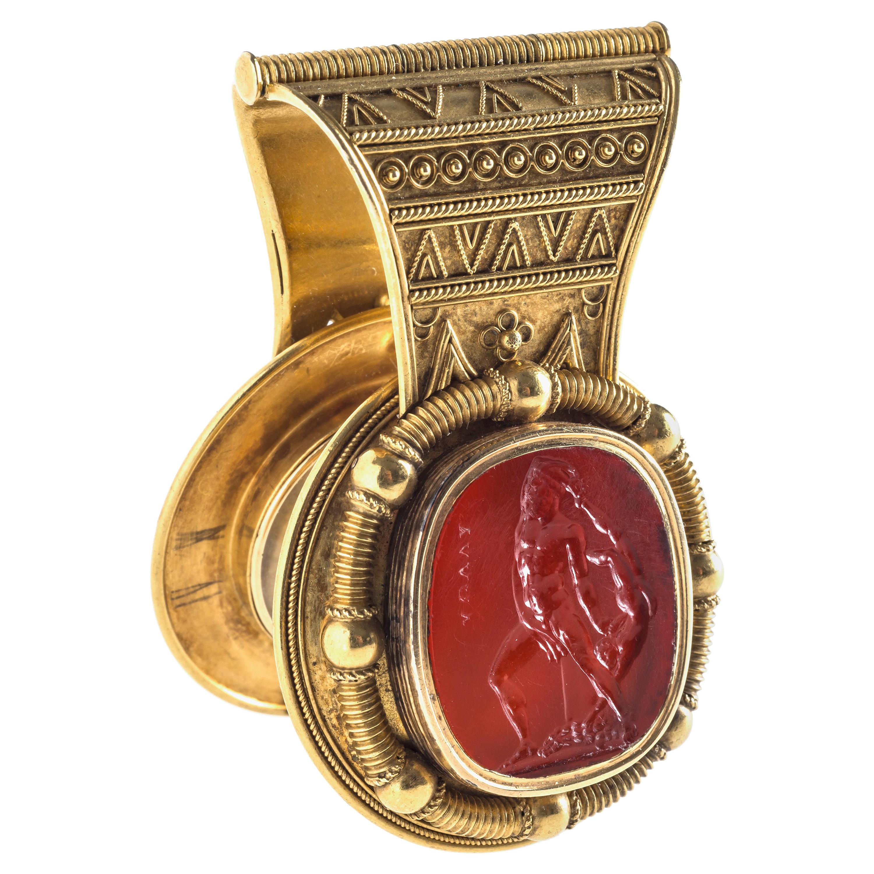 Golden bulla worked in 18K in the neoarchaeological style with a carnelian intaglio of Hercules and the boy Telephus. The hinged bulla can be opened to reveal a glass locket on the inside. The intaglio is set in a golden frame surrounded by tubular