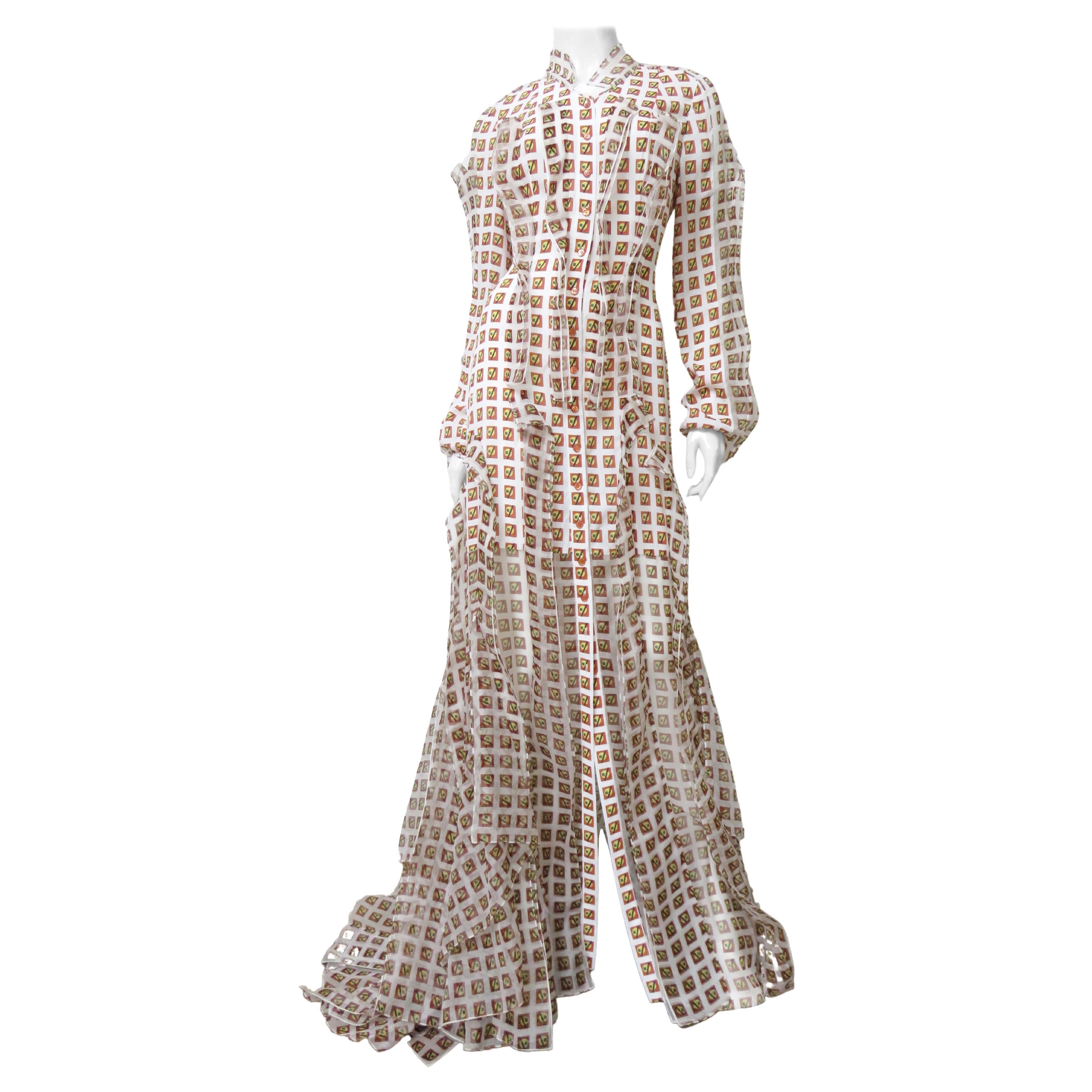 Uno splendido abito in seta di Carolina Herrera di colore bianco con una stampa geometrica a quadri arancione, gialla e verde. L'abito è semi-aderente, con maniche lunghe e piene che si raccolgono ai polsi e un colletto alto.  Si abbottona sul