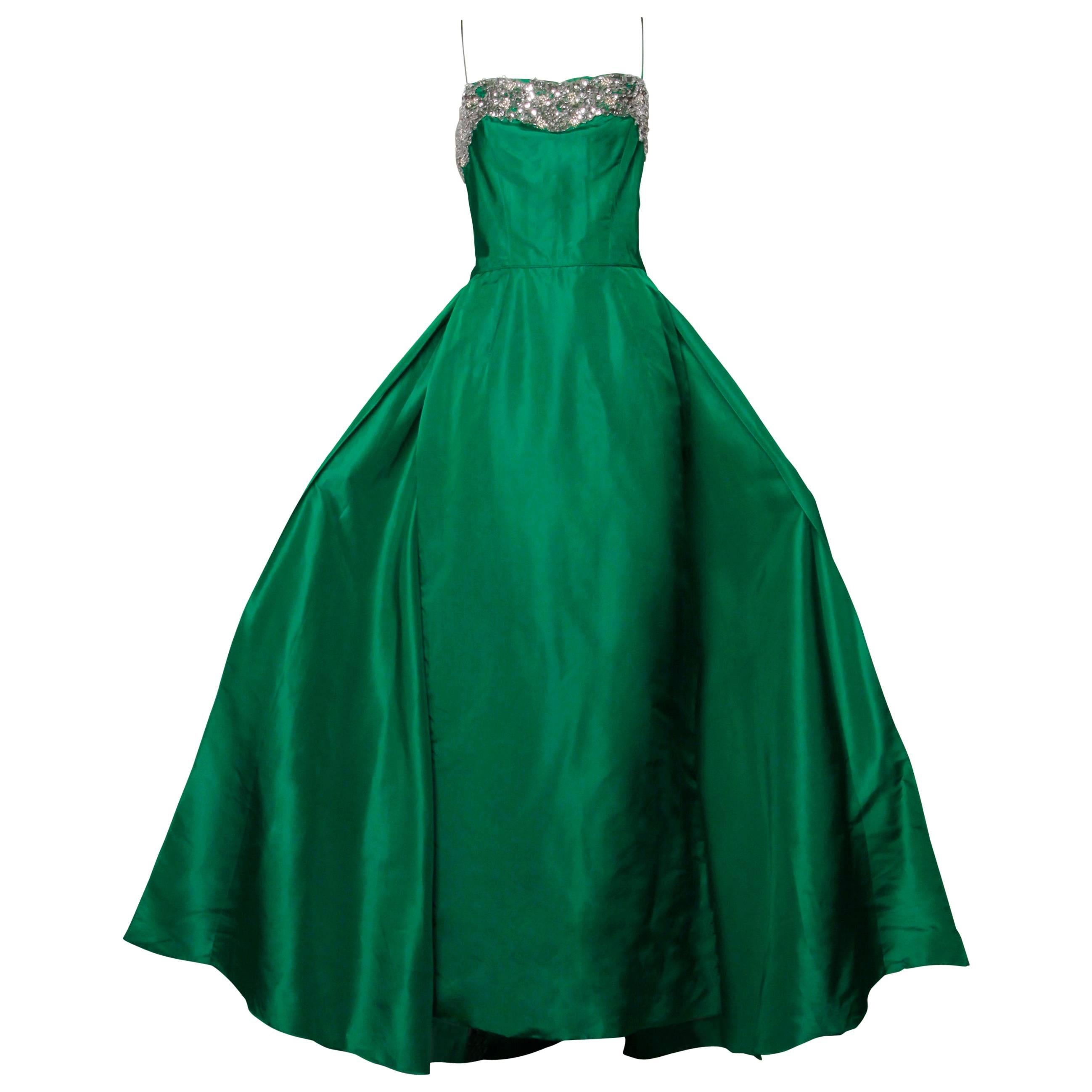 Incredible vintage 1950s formal gown in emerald green silk. The dress is fitted and features a massive back train, tiny nipped waist and beaded bust. Boned bodice, spaghetti straps and rear metal zip and hook closure. Fully lined. The dress has no