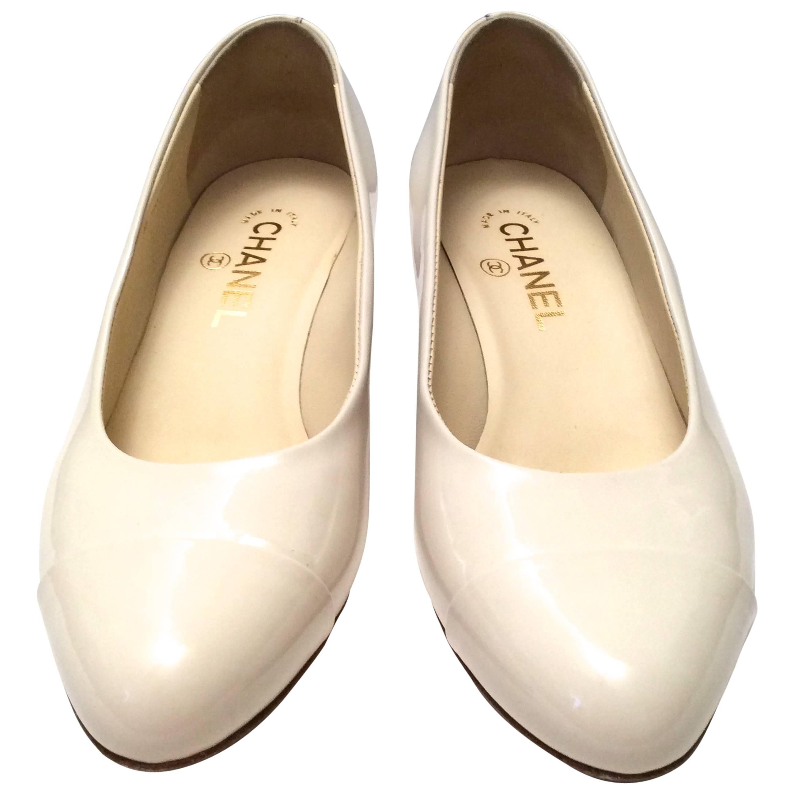 These gorgeous pumps from Chanel are a magnificent example of the simplicity and the artistry in the design of a Chanel shoe. They are patent leather in a cream white tone with embossed flowers around the exterior of the heel. There is a gold tone