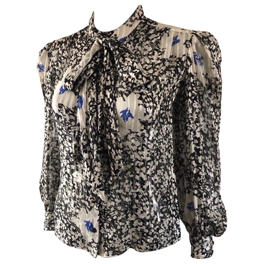 A beautiful classic, never out of style pussy bow blouse by designer David Hayes. The silk print is a lovely floral black and white with bright blue accents. Scarf is attached to the collar, but can also be tied as a long ascot or wrapped as a