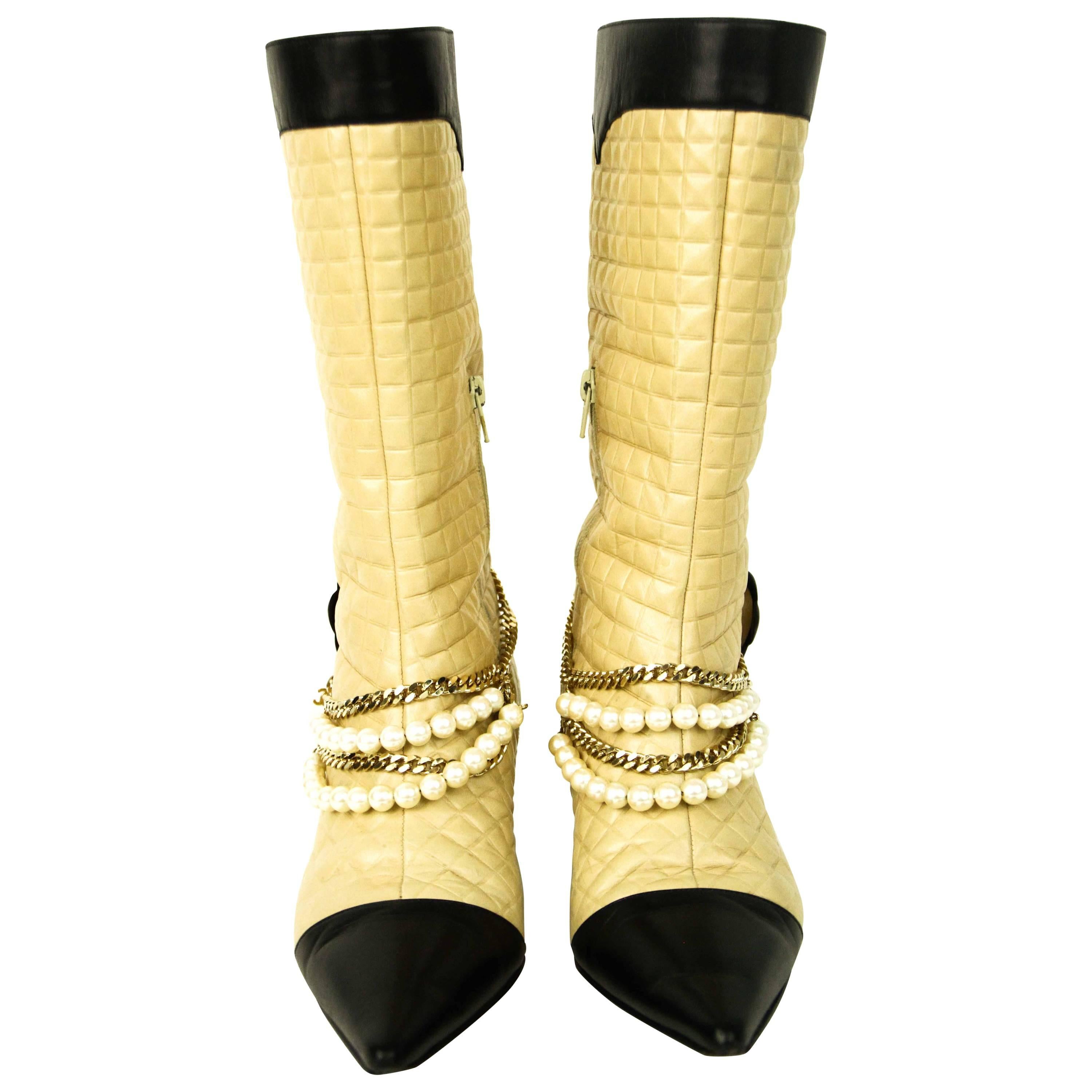 Offered is an authentic and pre-owned  pair of Chanel mid-calf quilted boots in 39.5.  Beige leather with a black cap toe embellished with a gold tone chain, pearls and leather camellia flower, chain is detachable.  Heel is two inches. 
Signs if
