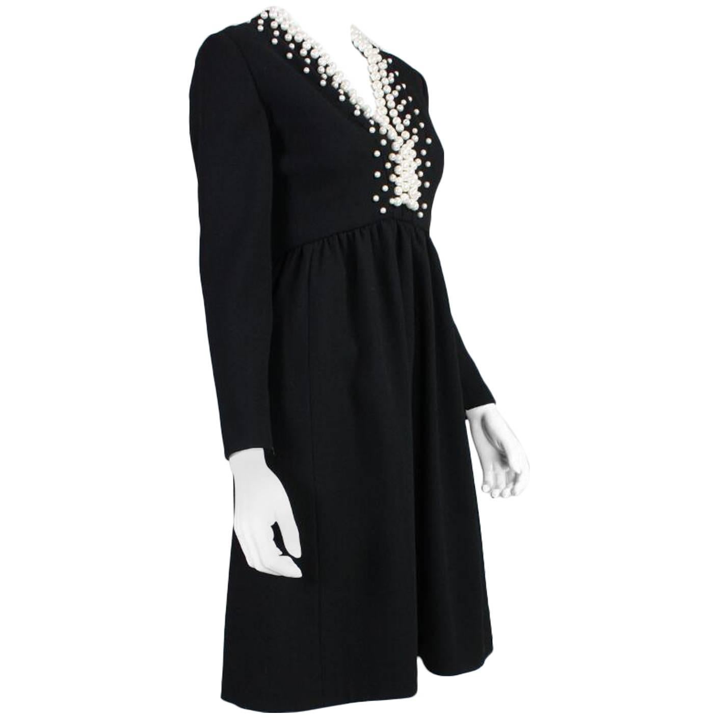 Vintage cocktail dress from Donald Brooks dates to the 1960's and is made of black wool crepe and features faux pearl detailing at the neckline and down the center back bodice.  There is gathering just under the bust in a V formation resulting in a