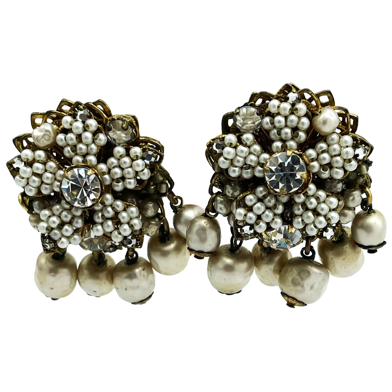 
Vintage ear clips from DEMARIO NY from the 1950s.
A round shape with a 5-petaled flower, these are set with tiny hand-crafted pearls. Larger rhinestone in the middle and at the tips of the petals. There are 6 movable beads hanging at the bottom.
A