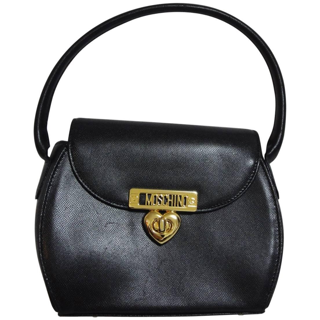 Vintage MOSCHINO black leather handbag, oval shape purse with golden logo motif. For Sale