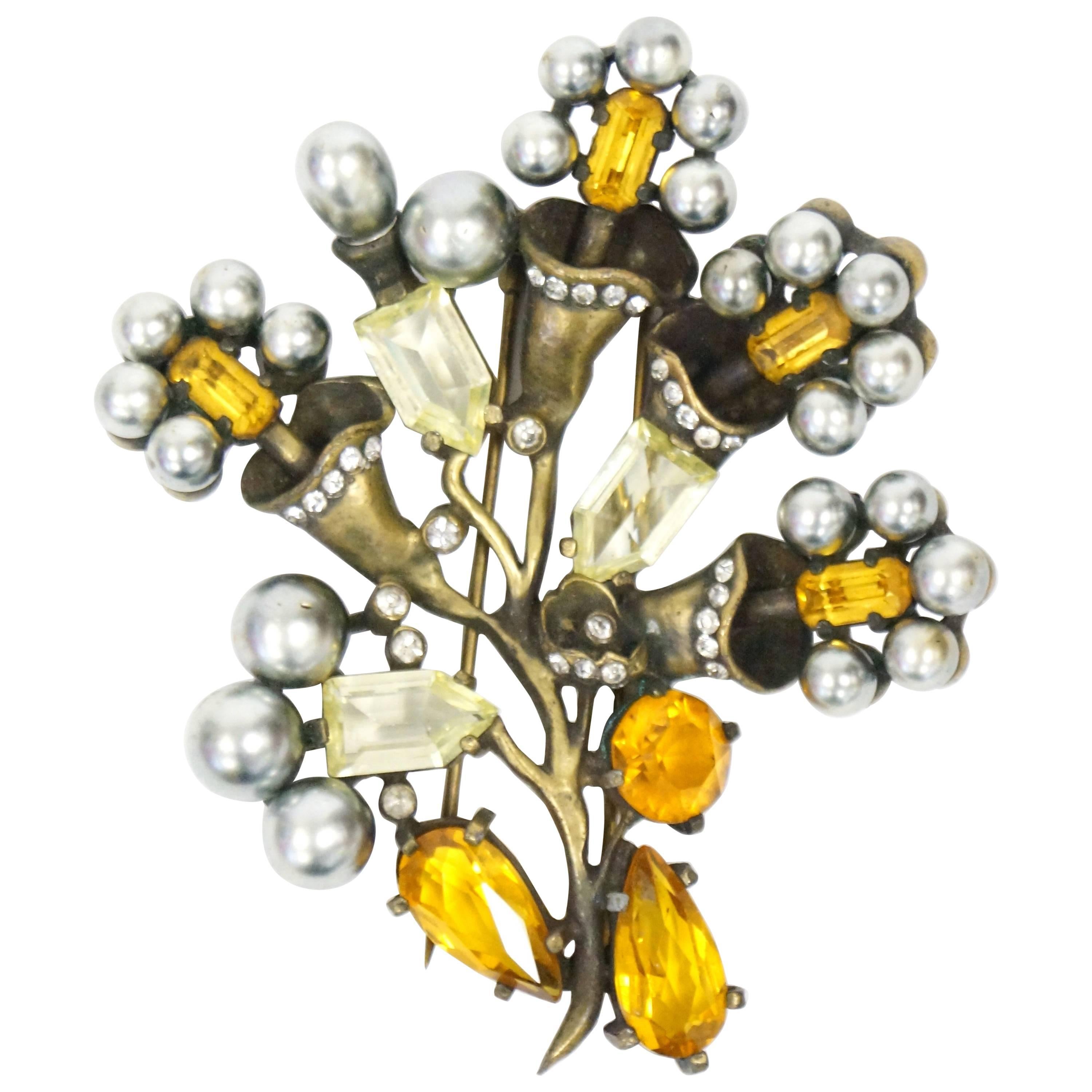 Beautiful rhinestone and faux pearl fur clip by Eisenberg. The four blooming flowers and two buds sprout from an antique brass stem. The flowers have emerald cut orange rhinestone centers, each sporting five grey pearl petals. Small round