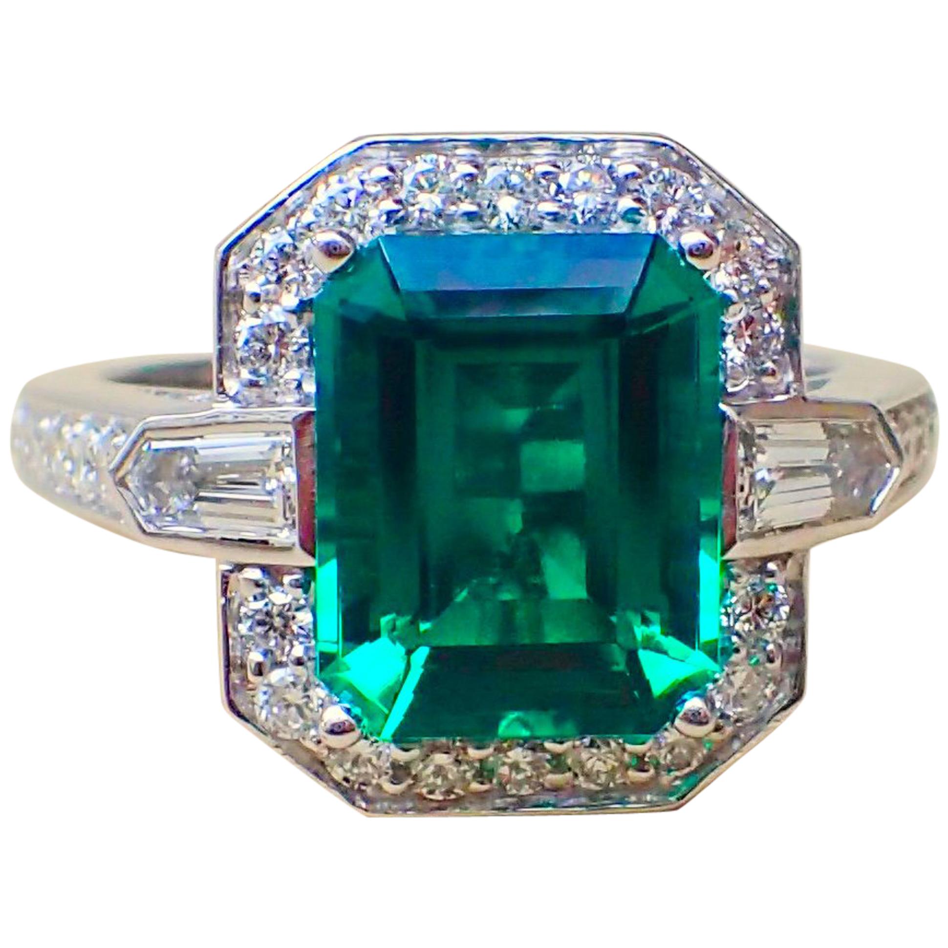 An 18k white gold ring is set with one (1) Emerald Cut Chatham-Created Emerald that measures 10mm x 8mm and weighs 2.83 carats with Clarity Grade VS-VVS and two (2) Bullet Cut Diamonds, one that measures 4.1mm x 2.3mm and weighs 0.14 carats with