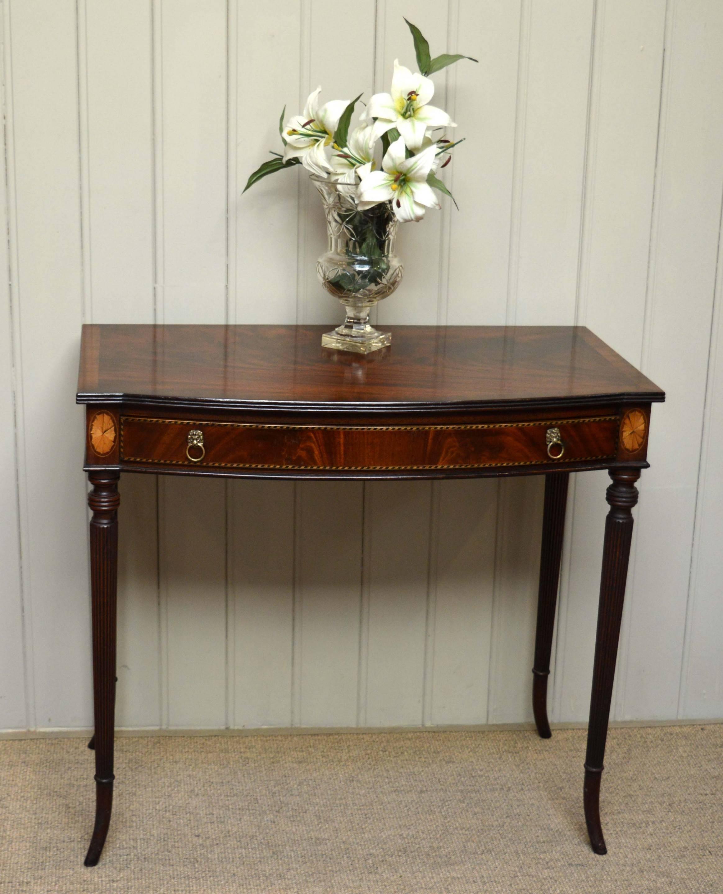Mahogany inlaid demilune table having a single inlaid drawer raised on reeded outsplayed legs.