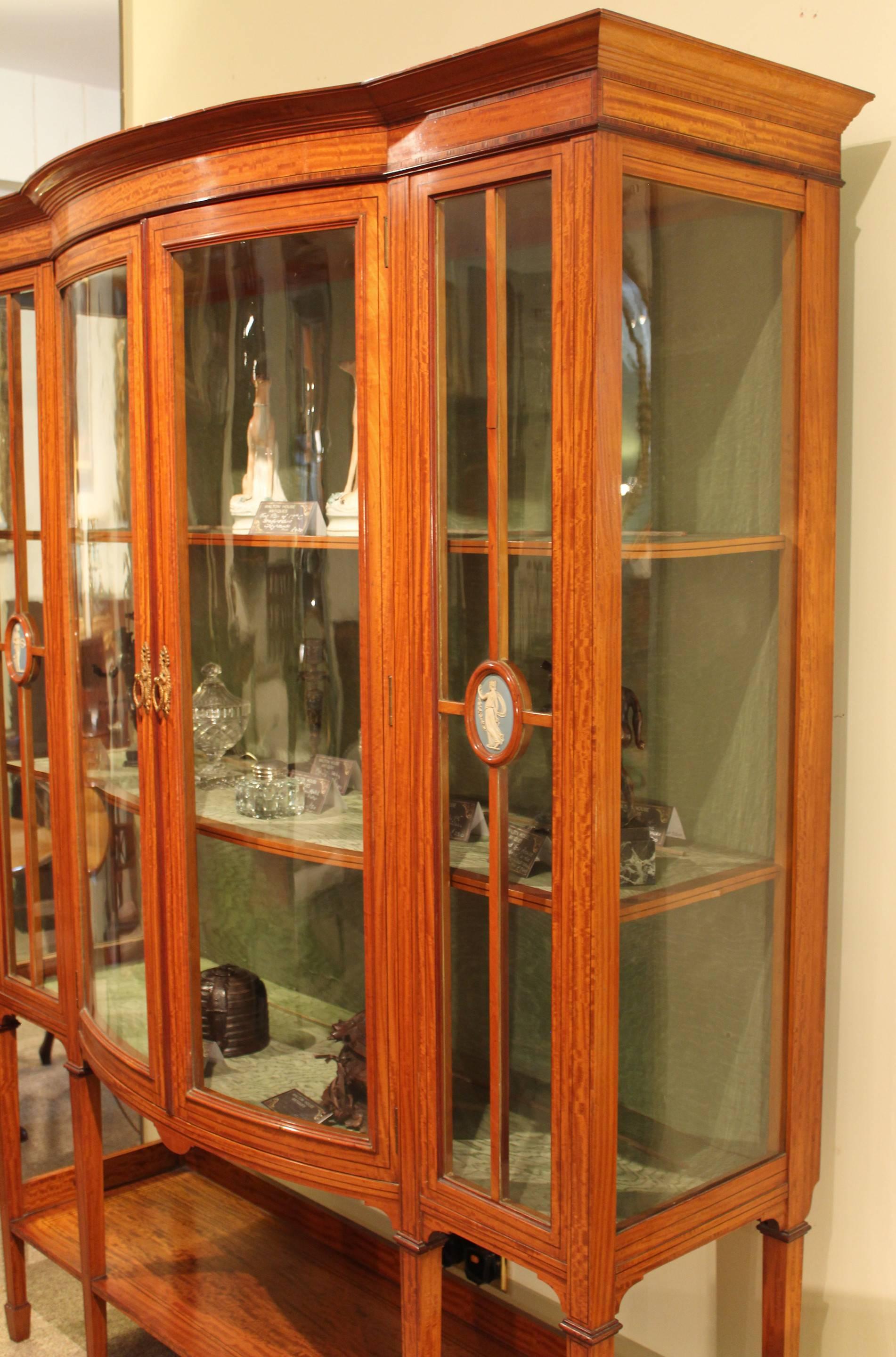 A good satinwood Sheraton Revival Edwardian display cabinet with bowed centre doors and charming Wedgwood plaques, circa 1910. 

All of the items that we advertise for sale have been as accurately described as possible and are in excellent