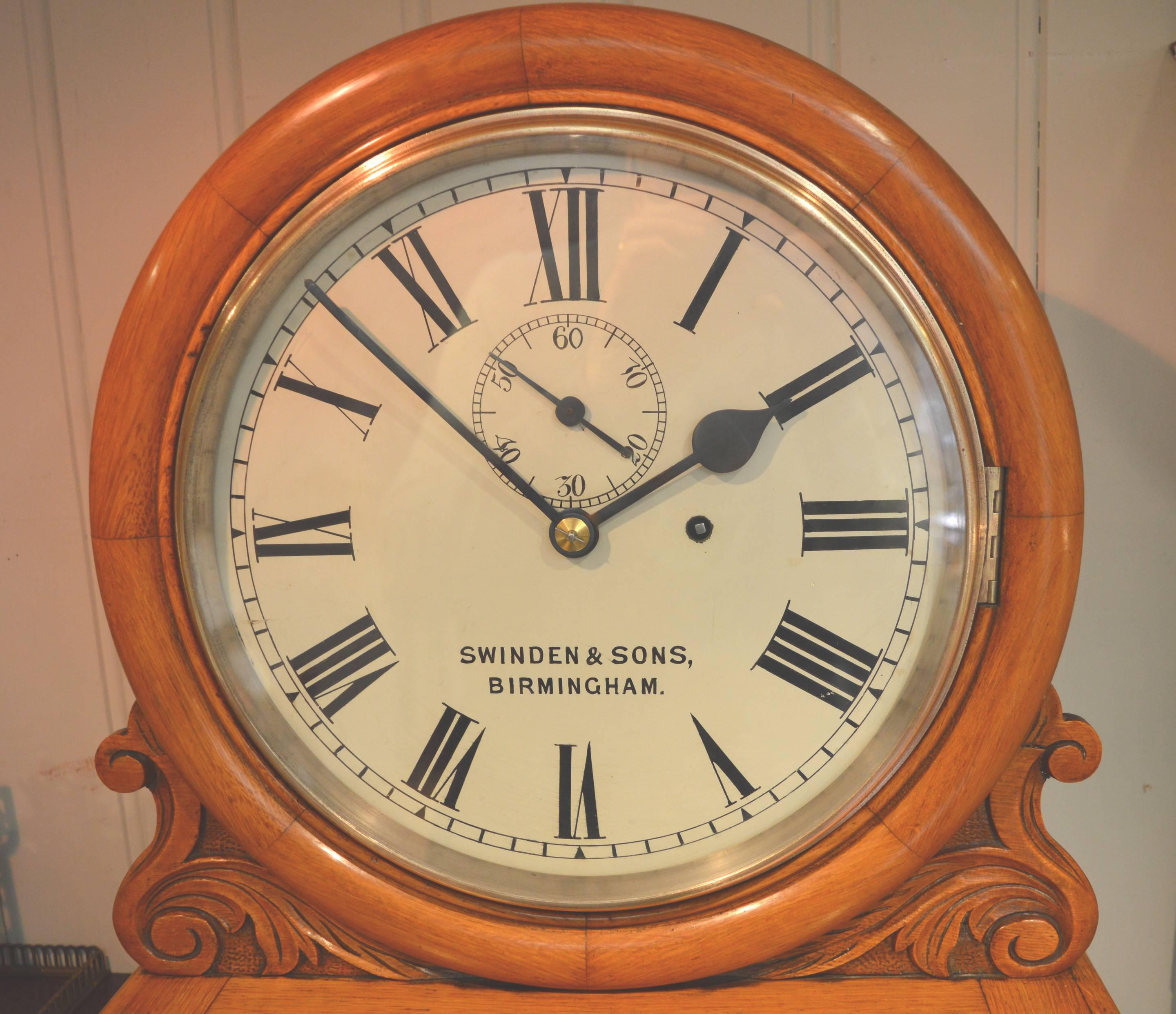 A high quality regulator wall clock probably from a commercial premises. It has a solid oak case, with a drumhead hood an carved shoulders. The long glazed door trunk has canted corners and a convex curved base. The 12 inch enamel door is signed by