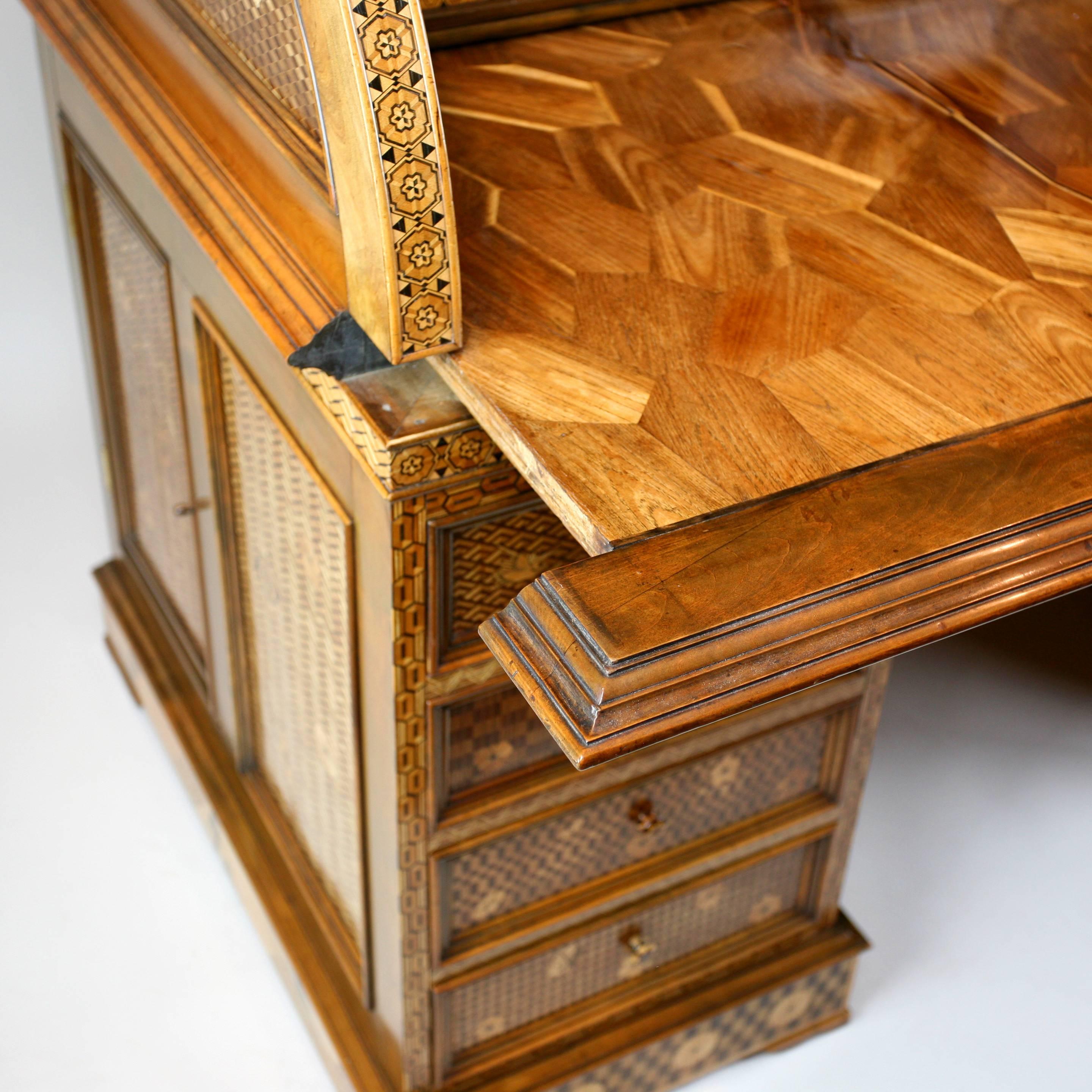 The lowest section with four drawers on either side of the kneehole and side cupboards, the central section with the roll top opening to reveal a pull out writing slide, pigeon holes, small shelves and drawers, the upper section with an elaborate