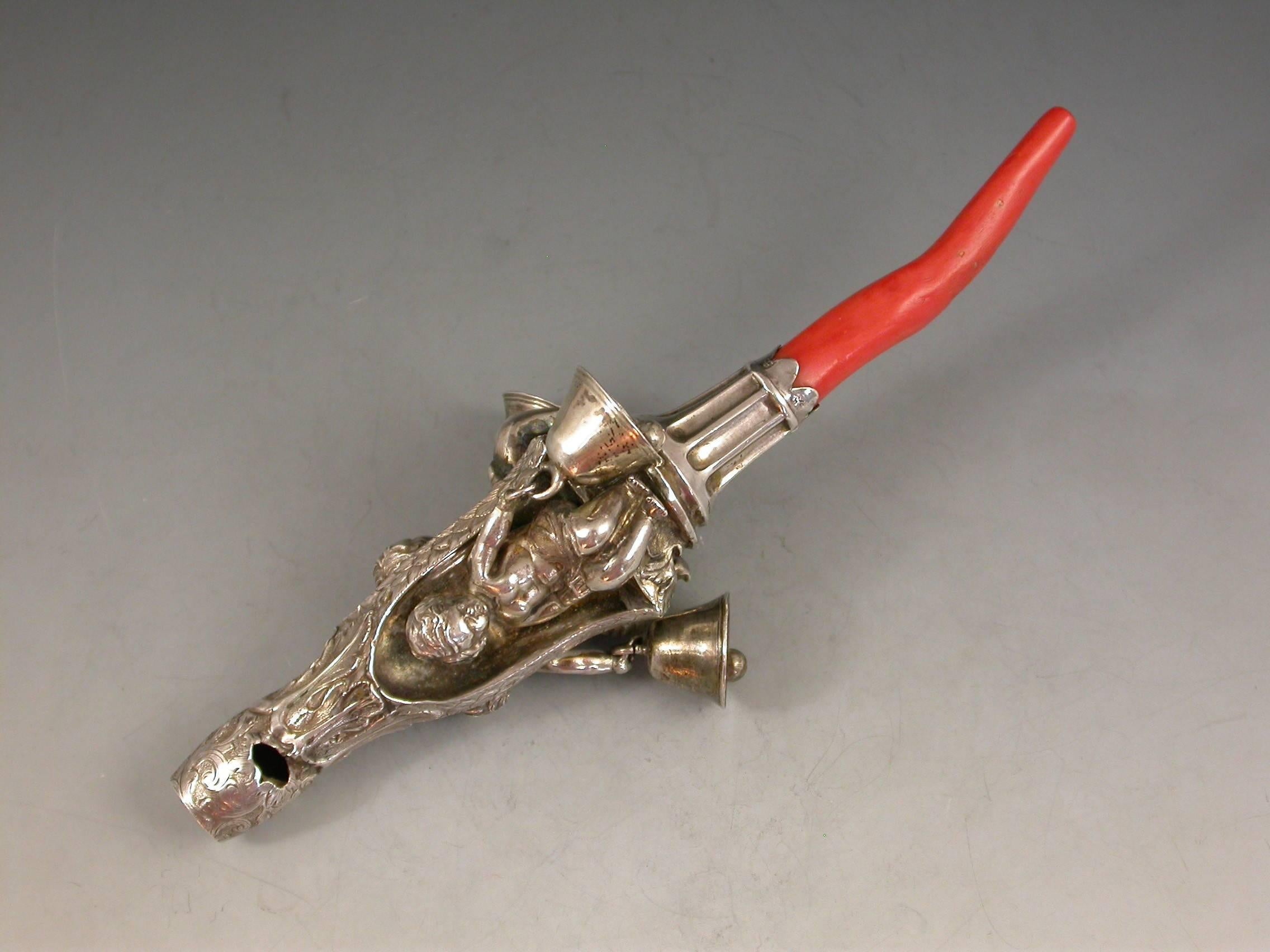 A very unusual Victorian silver Baby’s Rattle, the whistle with chased acanthus leaf decoration above three recessed arched alcoves inset with figures of naked putti each holding a pendant bell above a fluted column, terminating in coral stick