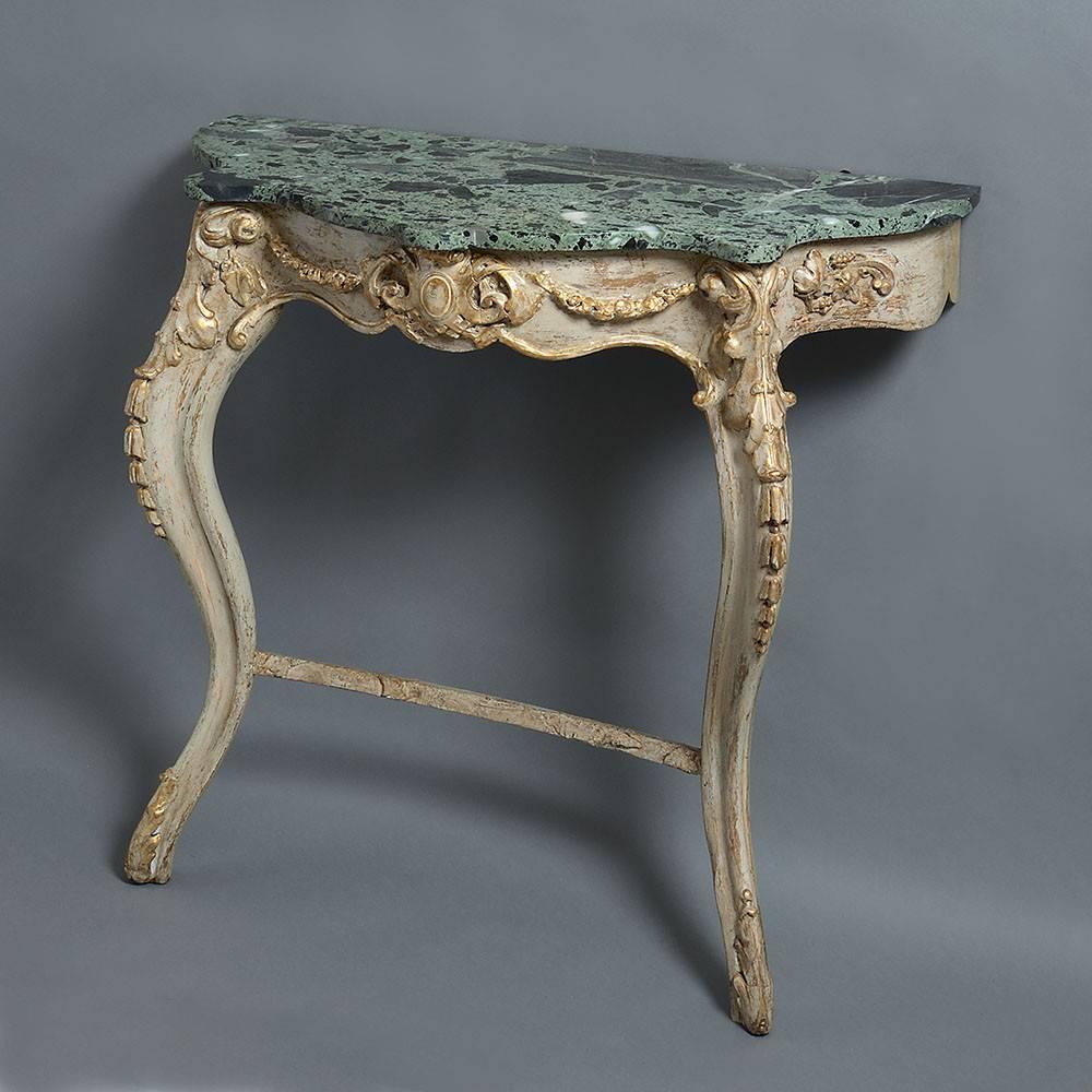 A mid-19th century painted and parcel gilded console table of serpentine form, the green veined marble top above a carved frieze with central cartouche, swags, stylised acanthus scrolls and husks, all supported upon two cabriole legs with a concave