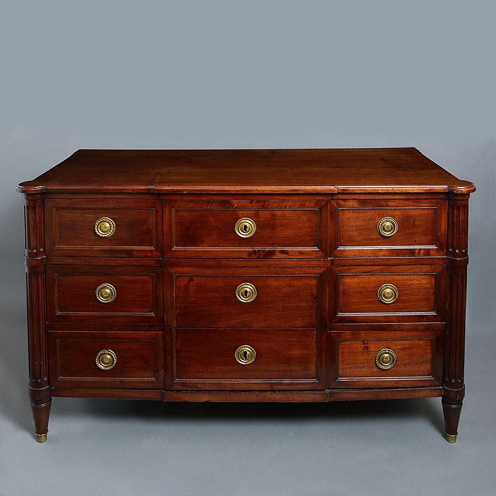 A finely figured late 18th century Directoire Period mahogany commode of generous proportions, the overhanging top above three short panelled drawers with medallion brass plates above two long drawers of the same, all set between fluted column ends