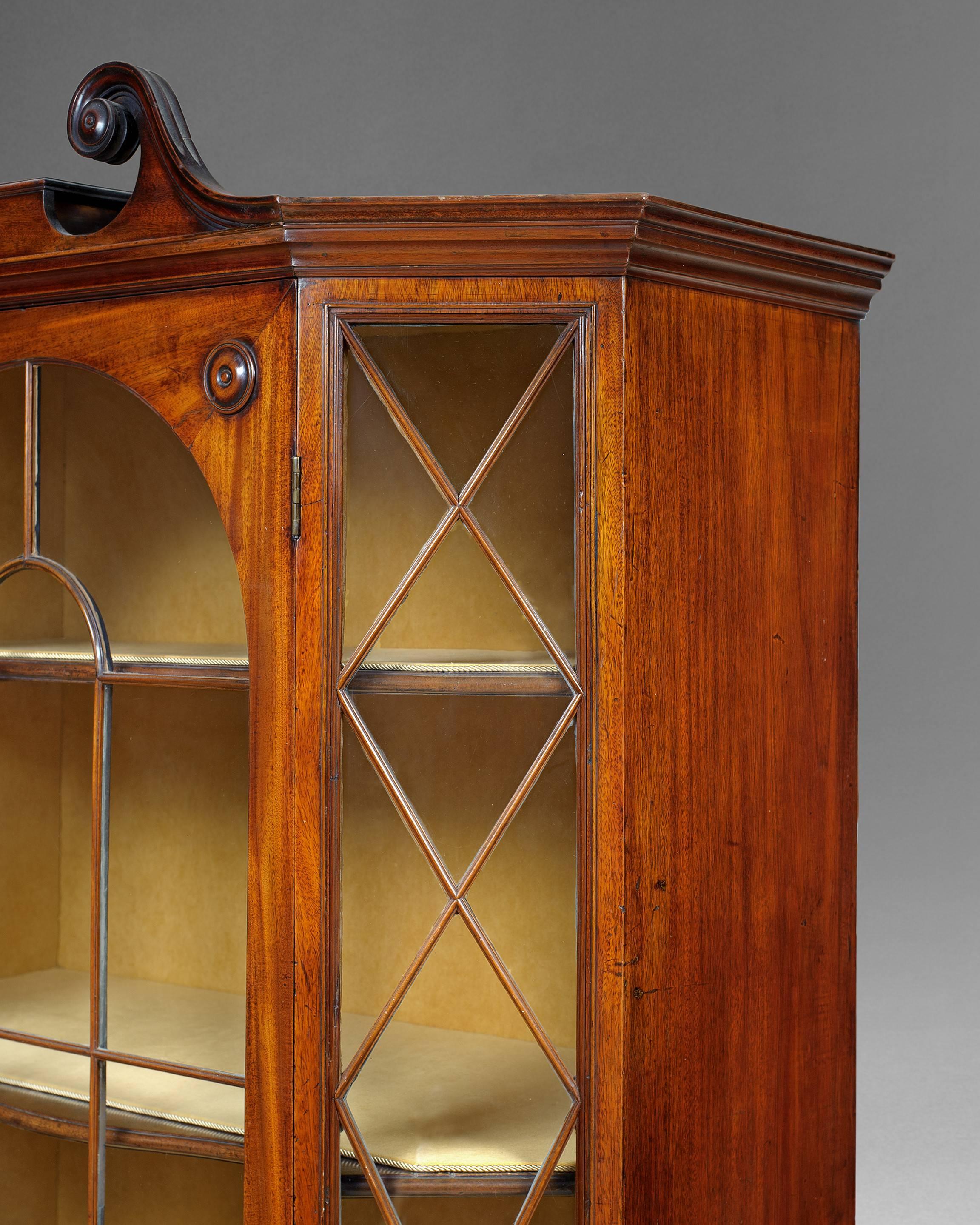 An important George III period mahogany hexagonal display cabinet, the top with a scrolling swan necked pediment above the stepped, moulded cornice, the upper part with a central glazed Venetian window door with arched astragal glazing bars and