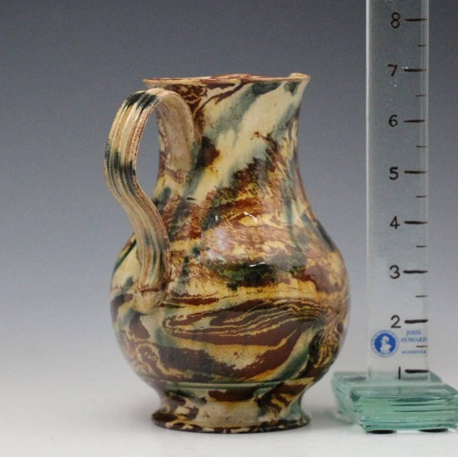 A fine example of Staffordshire pottery agateware from the mid 18th century. 
The jug is marbled in dark brown and blue below honey coloured shades and has a strap handle with the classic pinched lower terminal kick. 
A rare example of the early