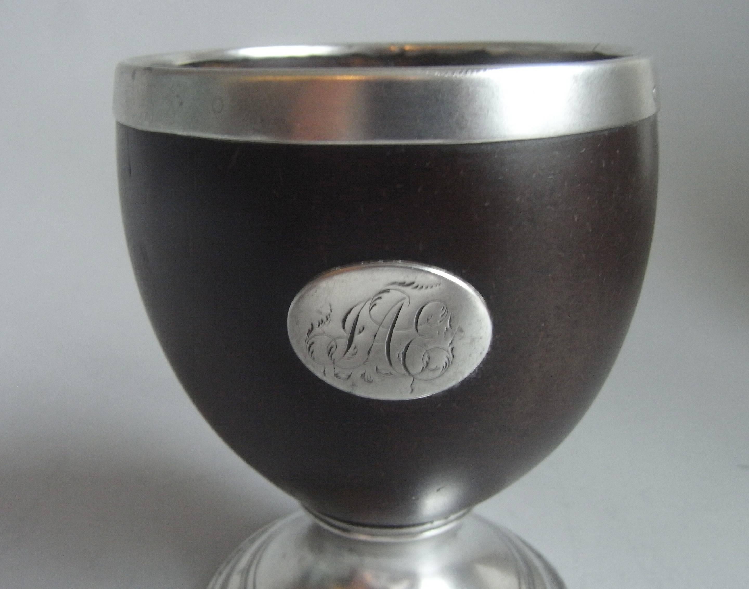 The Coconut main body stands on a stepped domed silver foot which is decorated with reeding. This example has a plain silver rim and the front also displays an oval disc cartouche engraved with a set of contemporary script initials. The coconut is