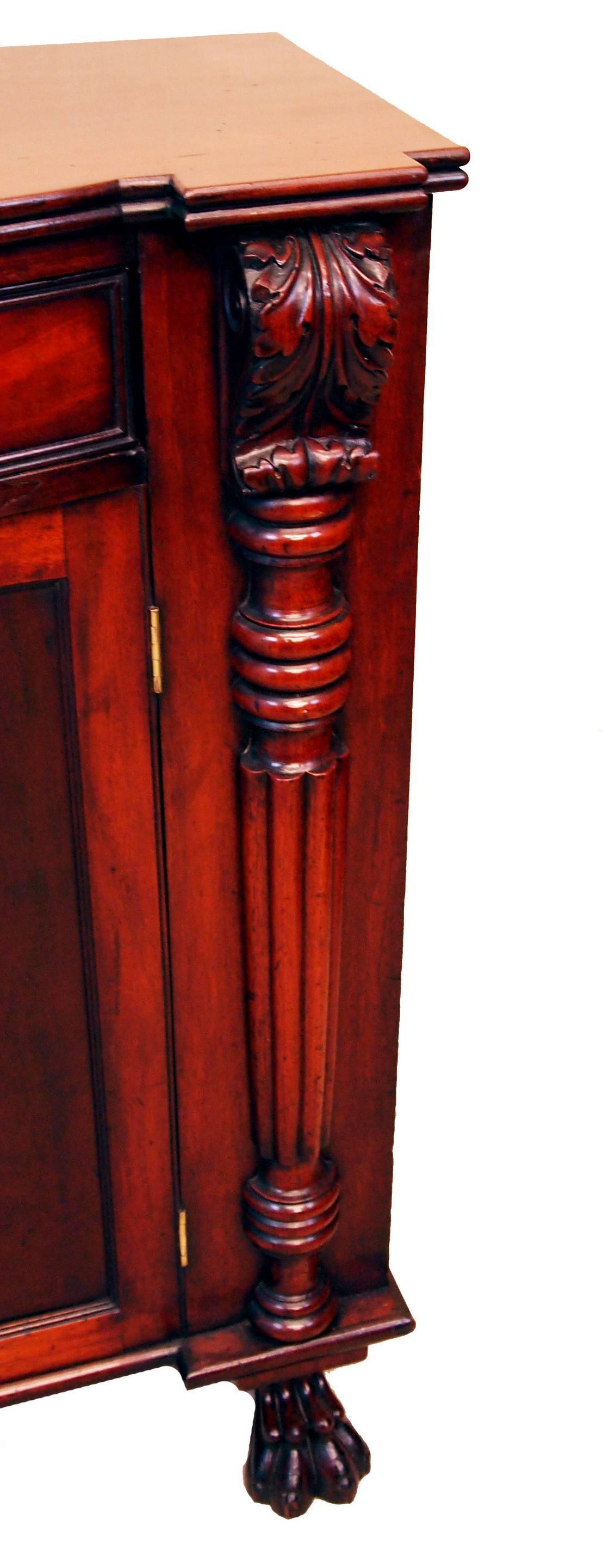 A good quality early 19th century mahogany side cupboard having bowfronted frieze drawer retaining original turned wooden knobs above well figured panelled cupboard doors flanked by very well carved scrolling pilasters and elegant half turned reeded