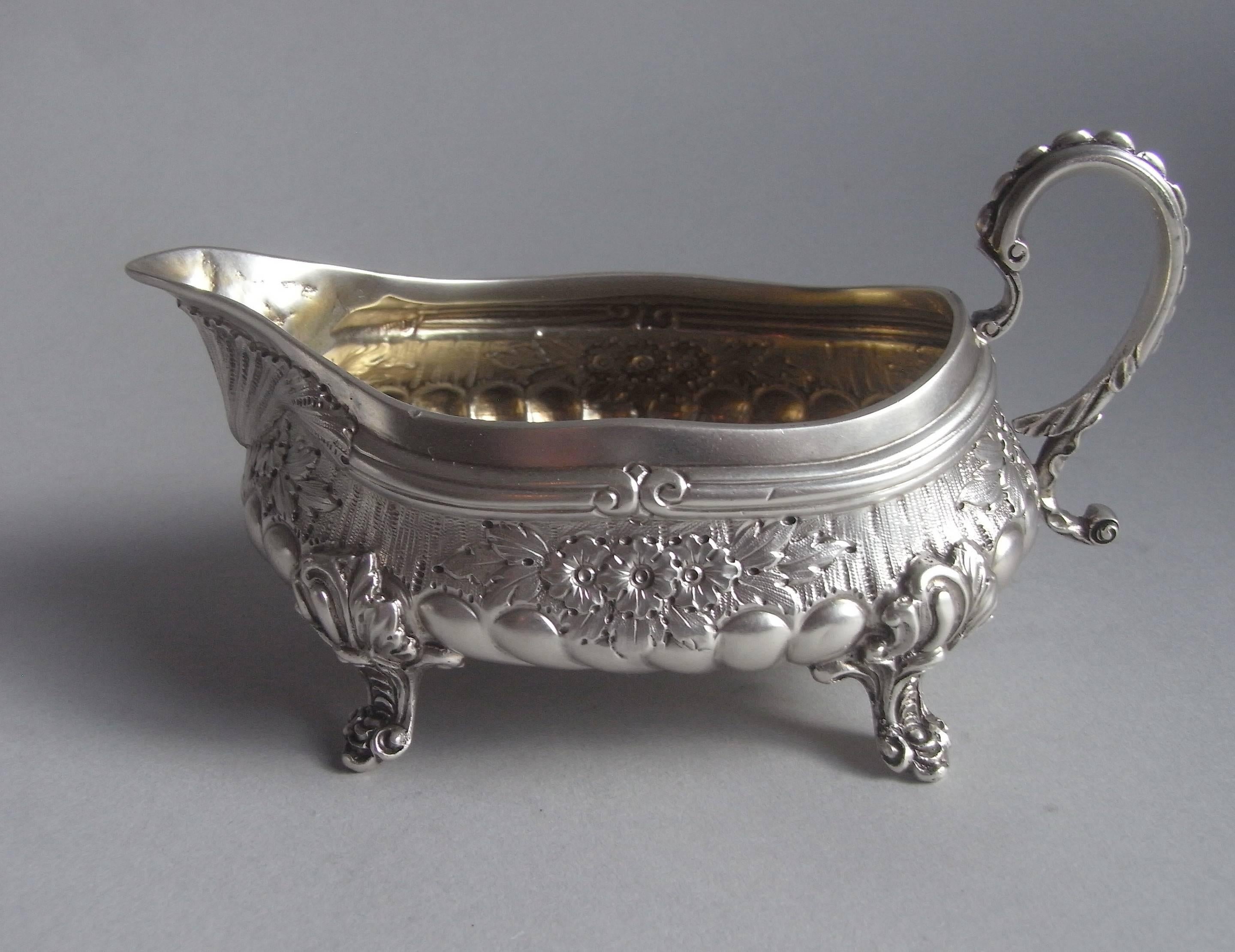 The cast cream boat is of a very unusual design in the manner of Paul de Lamerie. This piece stands on four scroll feet attached to the sides with foliate mouldings. The main body has a very unusual shallow elongated form, with sparrow beak spout.