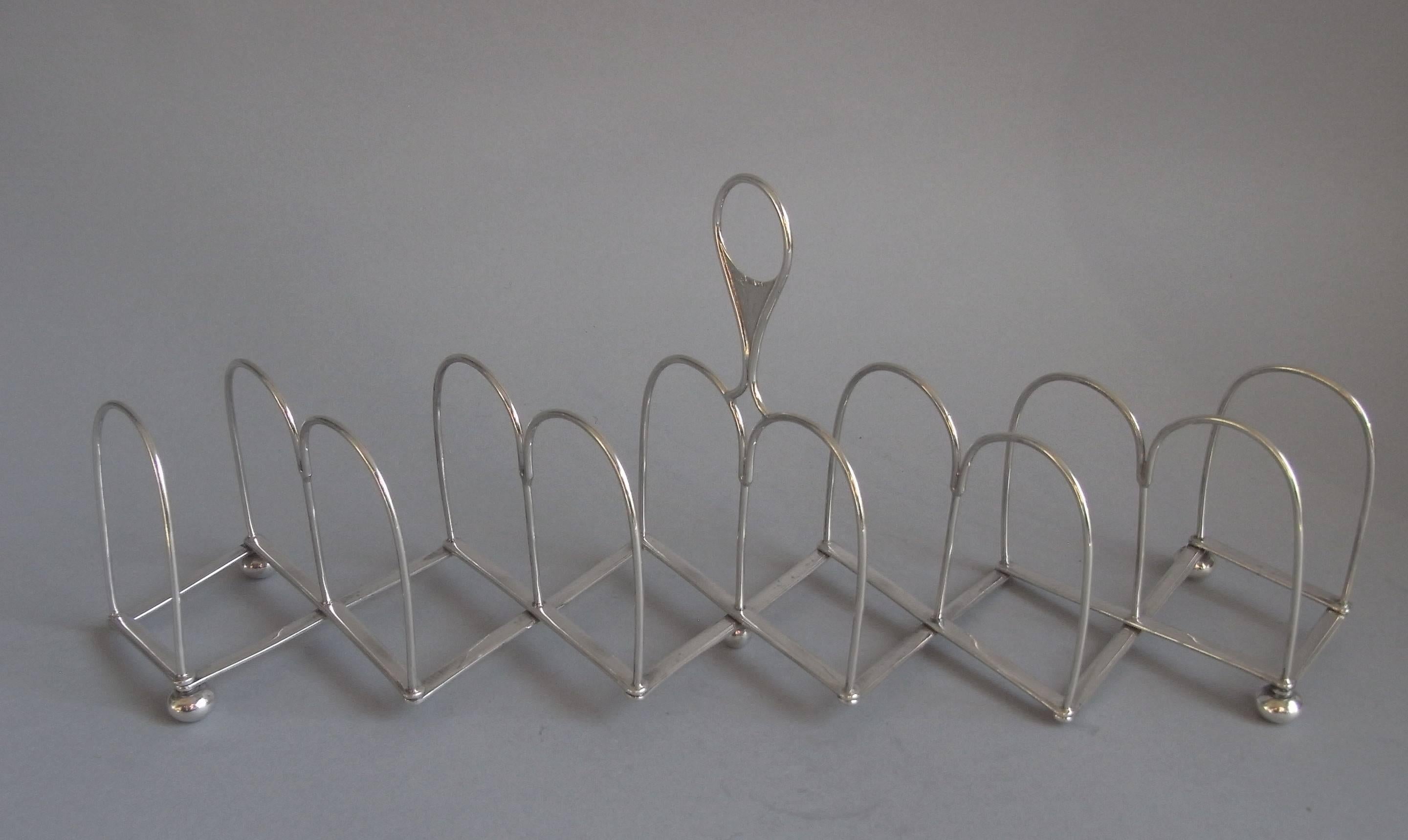 The Toast Rack is of the rare Concertina design and can extend to various sizes. This example stands on four ball feet and has a plain double arch design. It displays a raised central circular carrying handle. The base is engraved with R.C. & Co