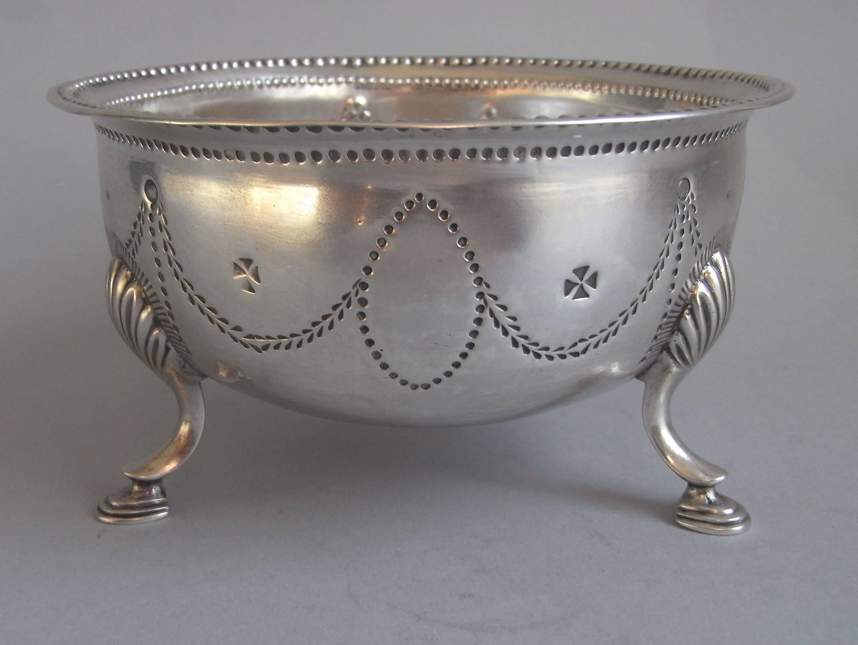 The Bowl is a typical Irish design and stands on three hoof feet, which are attached to the main body with raying shell mouldings. The everted rim is decorated with a double beaded rim. The sides are engraved with Classical stylised foliate