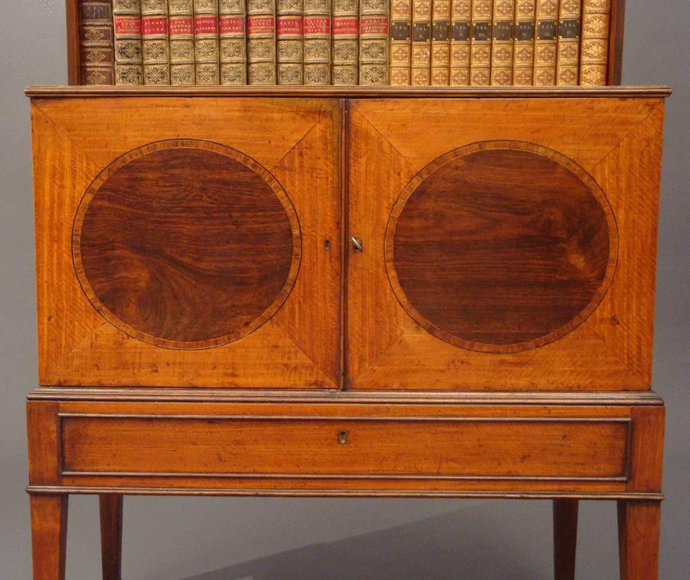 A George III Sheraton period satinwood dwarf bookcase, inlaid ovals in the doors and attractive cresting in original paint.