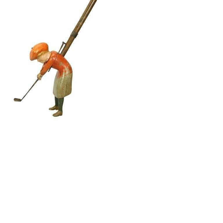 This indoor golfer is called Sissy Lofter. She is a wooden golfing figure attached to a wooden shaft and whose golf club will swing using a trigger mechanism. The figure stands 7” tall and is attached to a 30 ½” shaft. On the shaft just below the