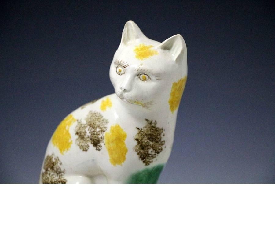A rare Staffordshire pottery figure of a cat seated on an oval base. 
This early creamware bodied figure is well decorated in under glaze oxide colors.
