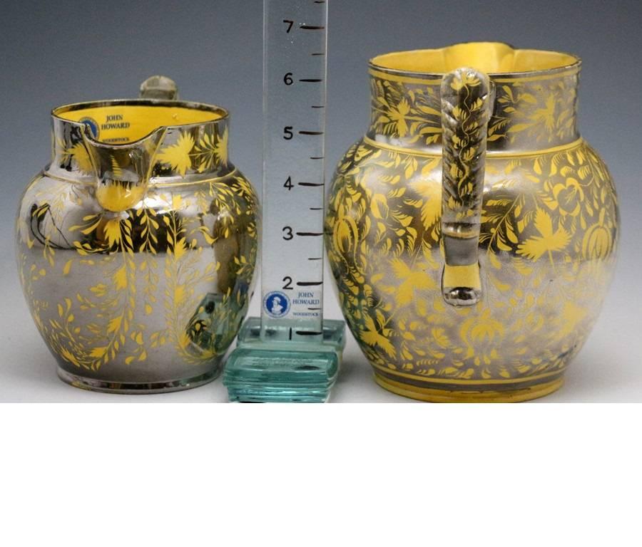 Two pottery canary yellow ground pitchers with silver luster resist decoration profusely and expertly applied. 
Produced in Staffordshire and Yorkshire in England and at Swansea in South Wales. 
Specific attribution cannot be ascertained.