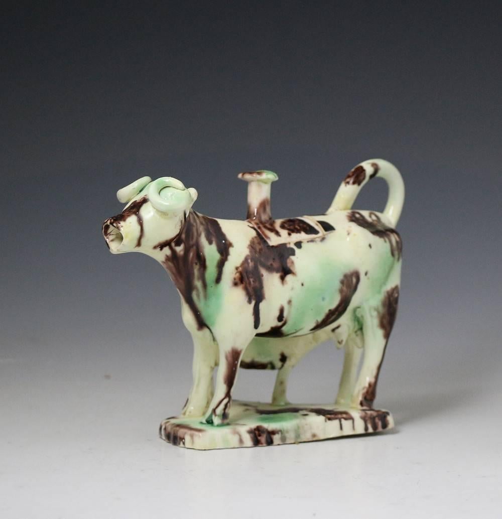 A rare creamware bodied pottery figure of a standing cow with suckling calf in the form of a creamer.
The figure is decorated in oxide colors with a good lead glaze and is probably the work of the master pottery Thomas Whieldon.