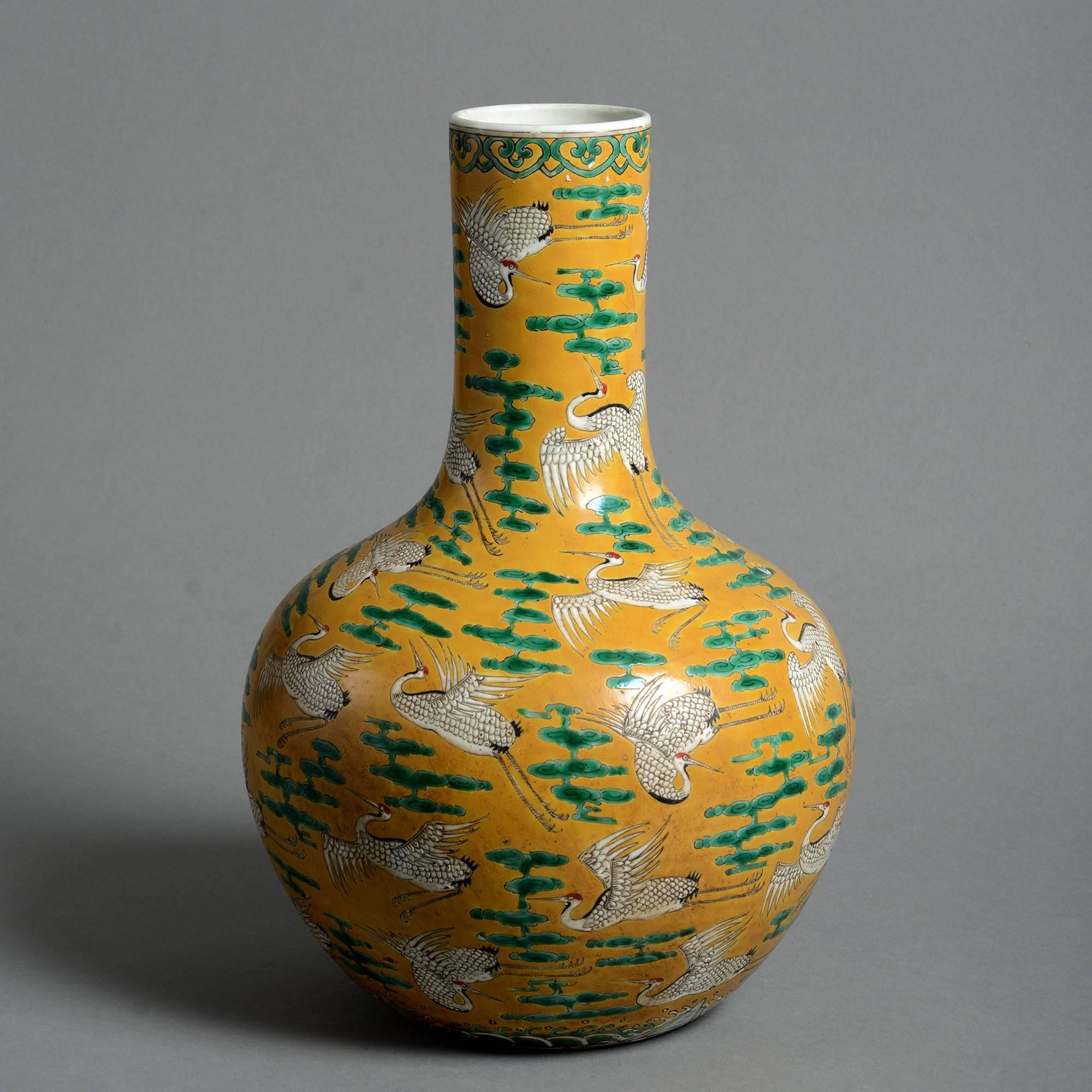 A late 19th century porcelain bottle vase, decorated throughout with cranes and clouds in white, red, black and green glazes upon a mustard yellow ground. With character marks to the underside. 

Qing dynasty, Guangxu period (1875-1908).