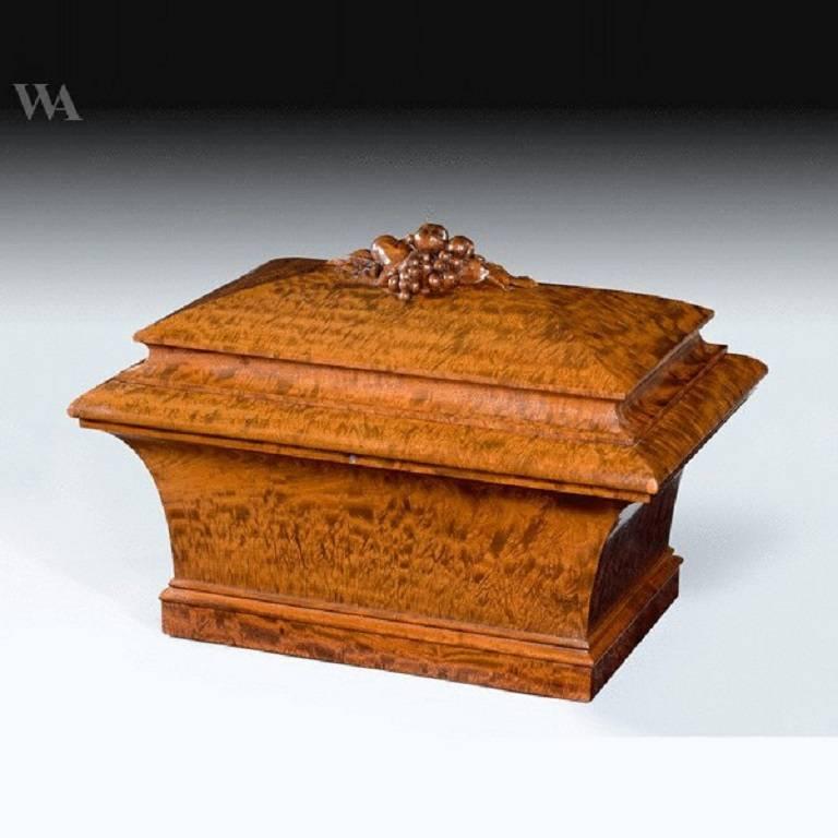 A William IV plum-pudding mahogany cellaret
of sarcophagus form with a hinged lid, surmounted by an apple and grape finial, the interior with fitted bottle compartments.