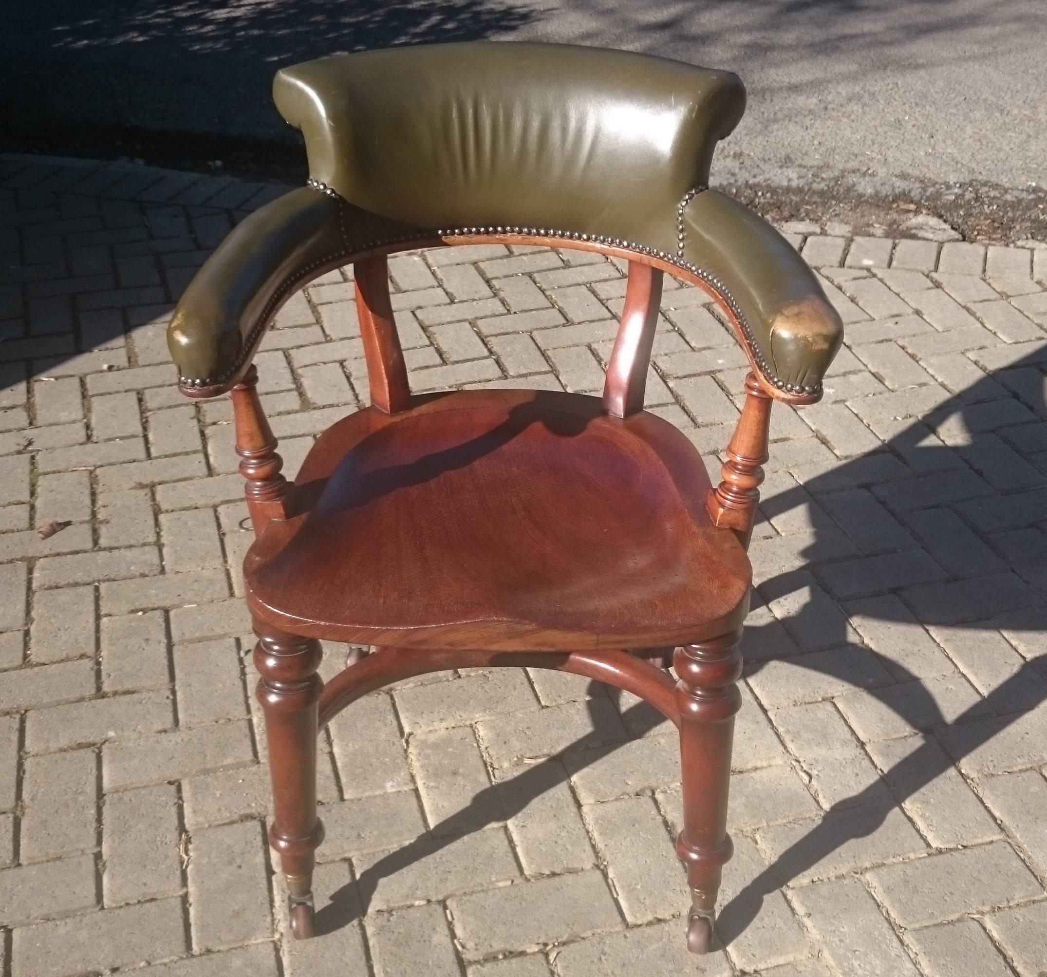 Antique desk chair, captain's chair or club chair standing on turned front legs and porcelain casters. This chair is an interesting design in that it has an exaggerated curve to the back legs, an inventive version of the H frame stretcher and