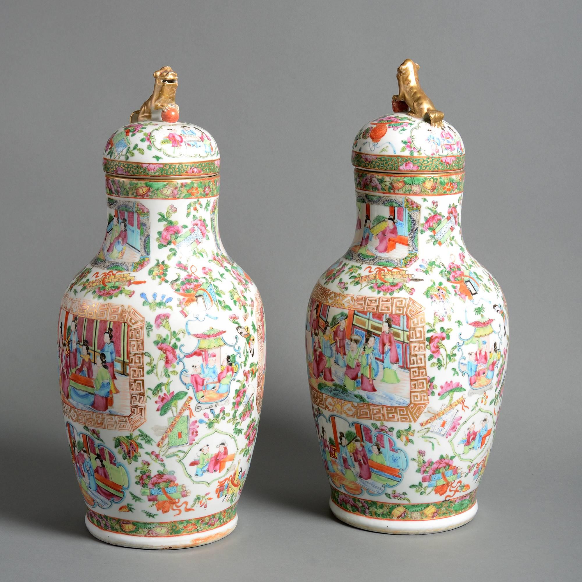 A pair of late 19th century Canton porcelain vases, decorated with panels depicting courtly scenes in famille rose glazes upon a white ground, the domed lids surmounted with gilded lions. 

Qing dynasty, Guangxu Period (1875-1908).

Condition: