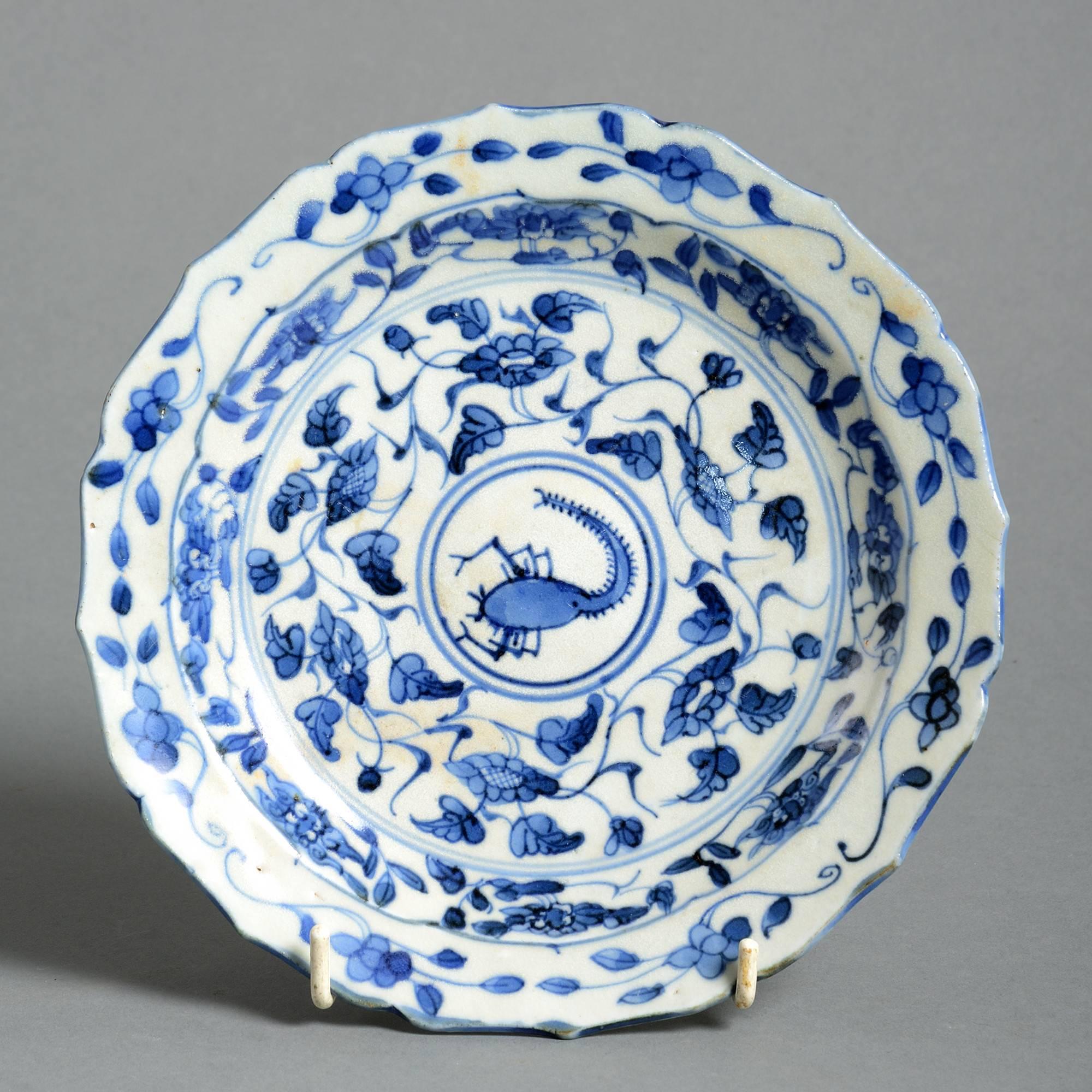 A mid-16th century blue and white glazed porcelain plate, having a shaped edge, with foliate decoration and depicting a stylized scorpion to the centre. 

Ming dynasty, Jiajing period (1521–1567).