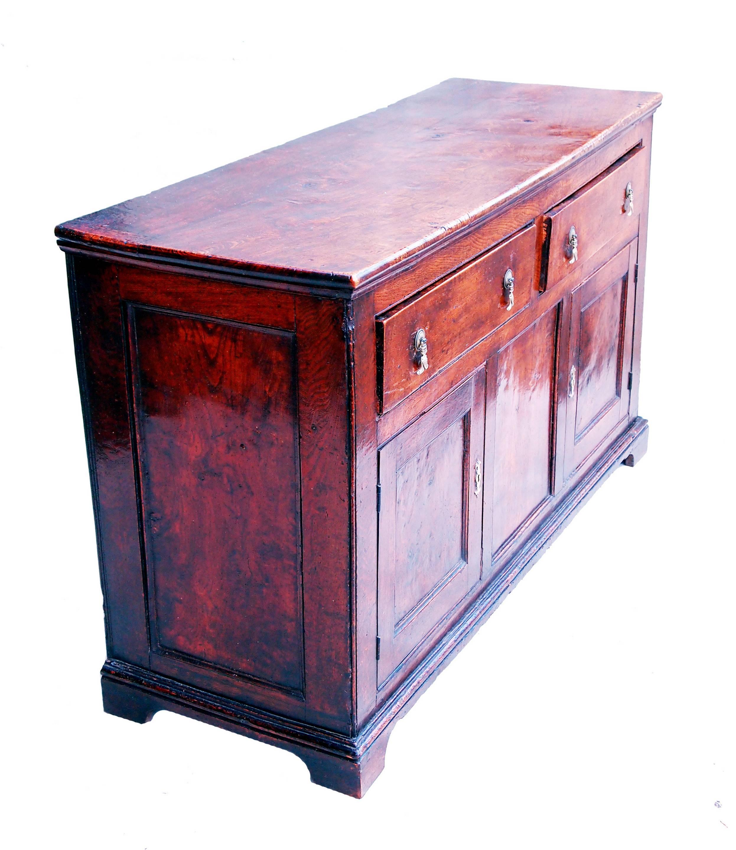 A charming 18th century elm dresser of exceptionally rich color
and patina, the superbly figured rectangular top above two short
drawers with later brass handles and two well figured panelled
cupboard doors raised on shaped bracket feet.