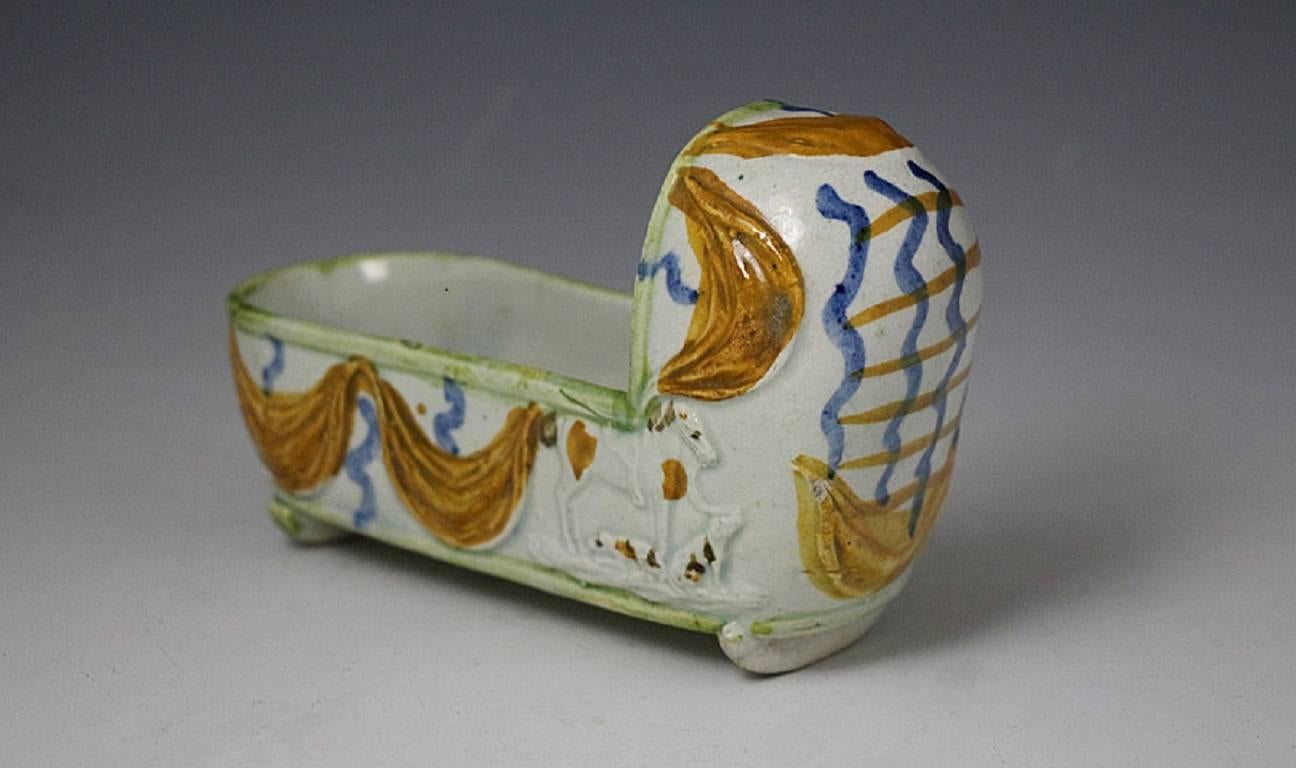 A fine antique prattware pottery pearlware crib strongly modeled with relief decoration, and unusual and rare feature, the addition of a horse and two dogs on the side panels.
The cradle is draped in ochre colored swags providing good decorative
