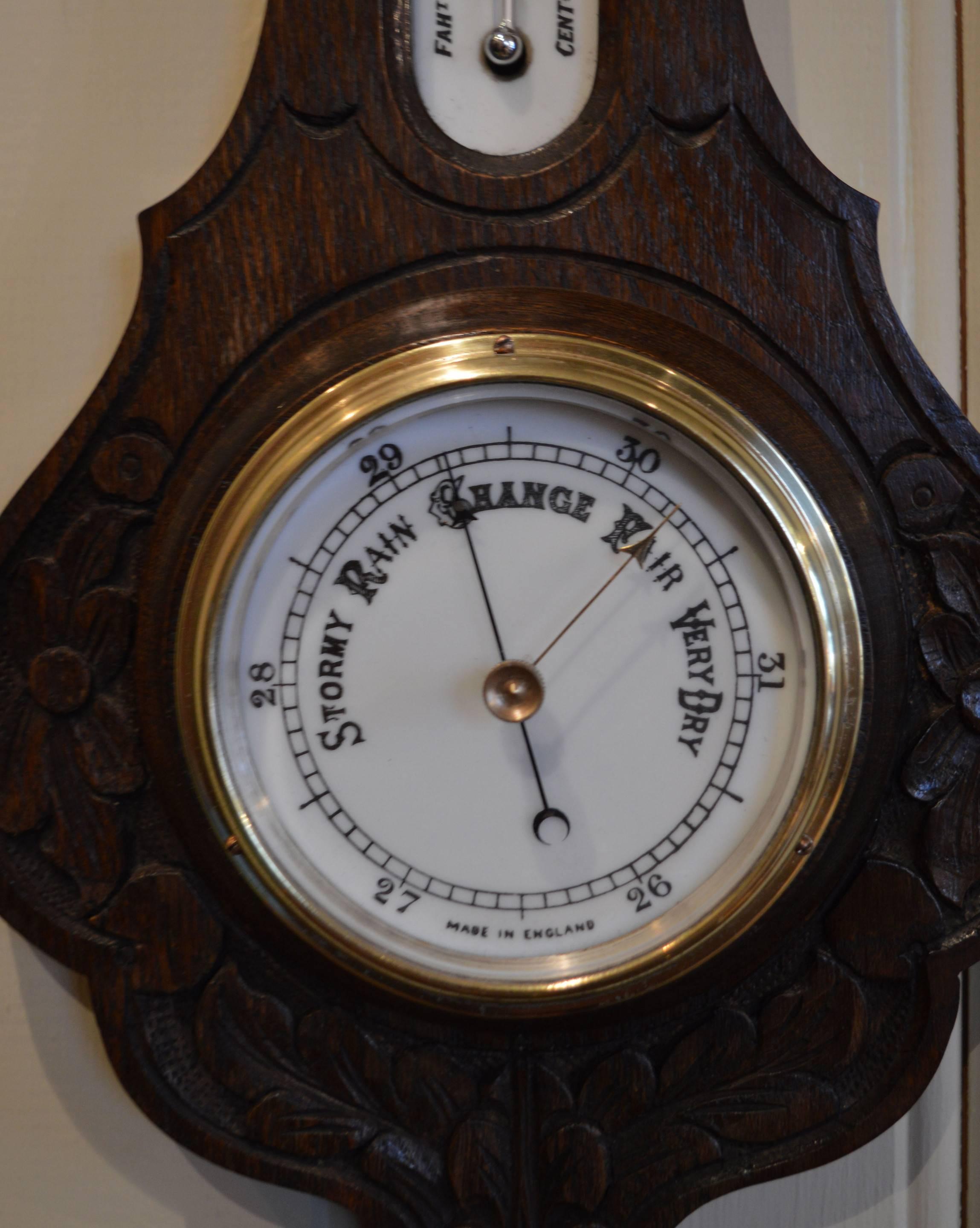 A solid carved oak wall barometer. It has a banjo shaped case, with a top milk glass thermometer window, a 4 inch milk glass dial with a bevel edge glass.