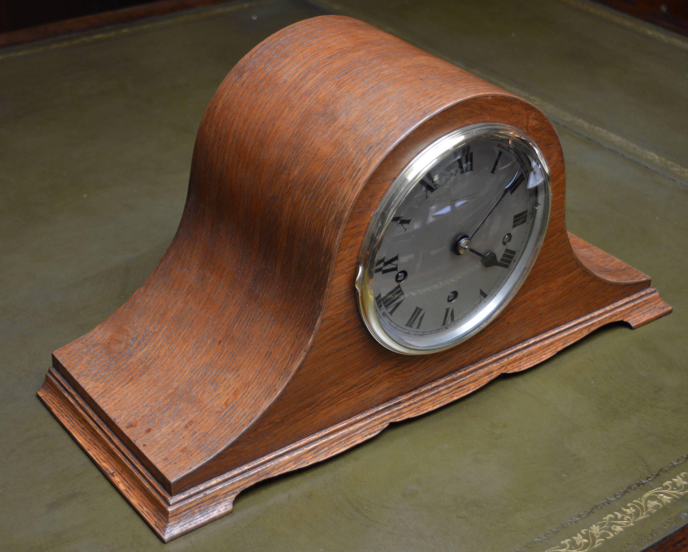 A good quality early 20th century mantel clock in the shape of a Napoleons hat. It has an oak case with a shaped plinth, a convex engraved and silvered dial signed by the original retailer Searle of London. It has a cast brass bezel with a convex
