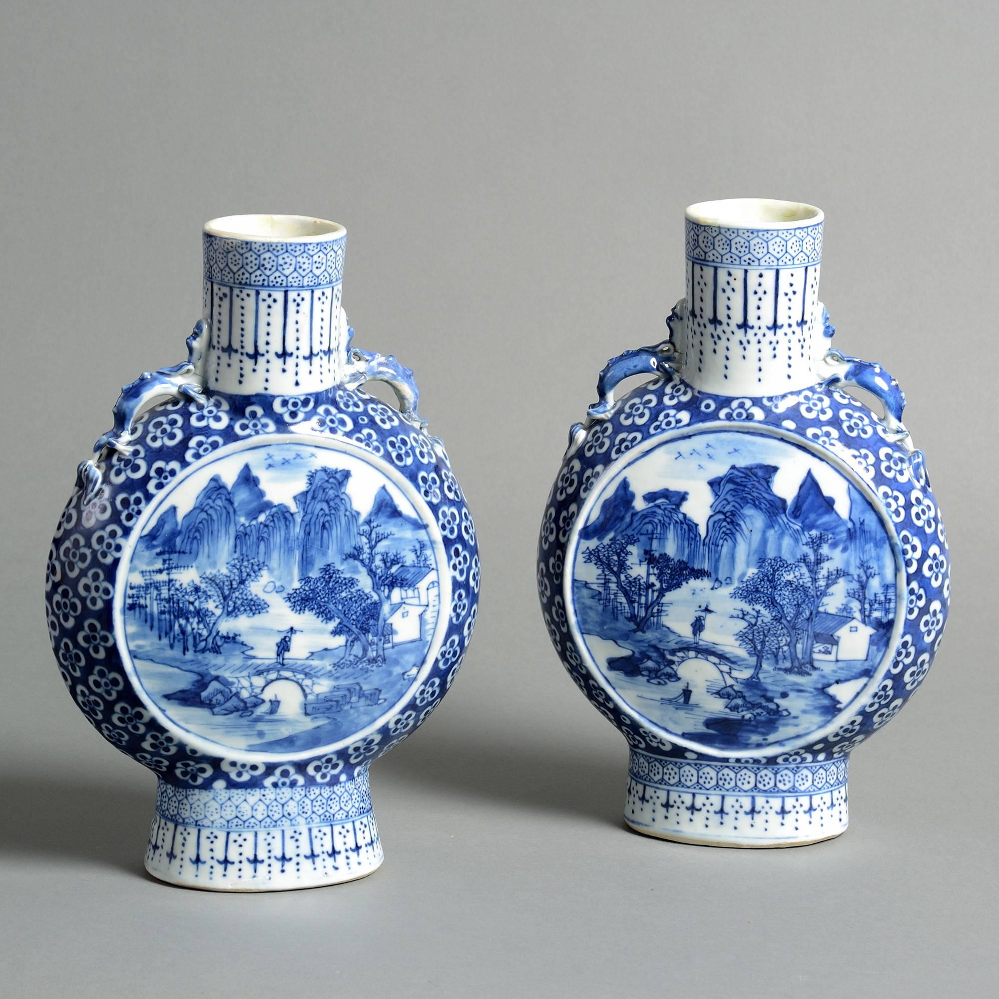 A pair of blue and white porcelain moon flasks, decorated with circular landscape cartouches upon a ground of prunus blossoms.

Qing Dynasty, Guangxu period (1875-1908).

Both necks restored; one with restoration to the body.