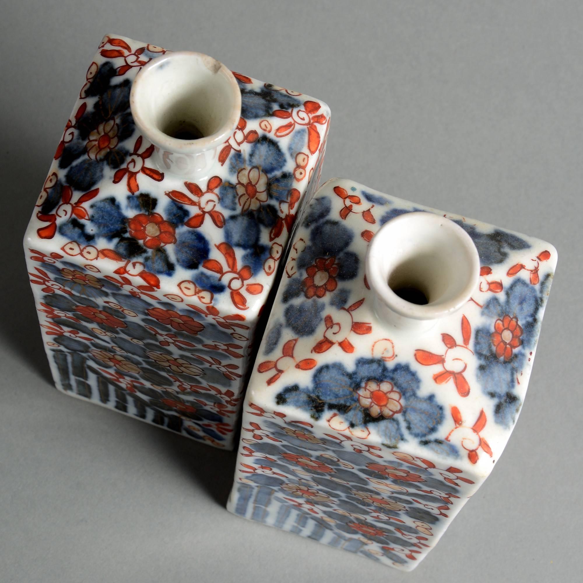 A pair of late 19th century porcelain flasks, of square form, the bodies with floral decoration in red, blue, black and gold glazes upon a white ground,

Meiji period (1868–1912).