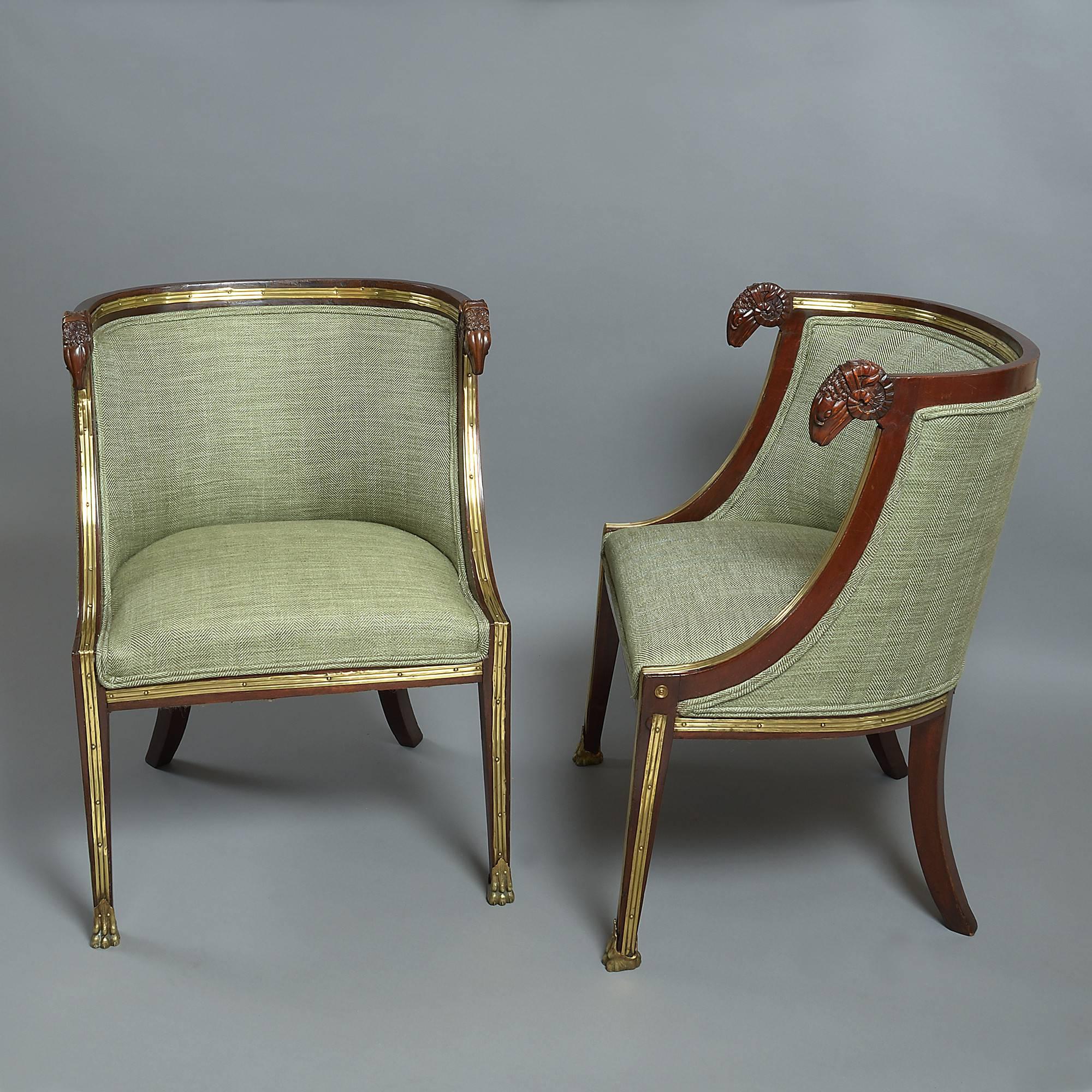 A rare and unusual pair of brass-mounted mahogany bergeres in the neoclassical, of tub form, having rams head armrests and raised upon square tapering legs with gilt metal hairy paw mounts.