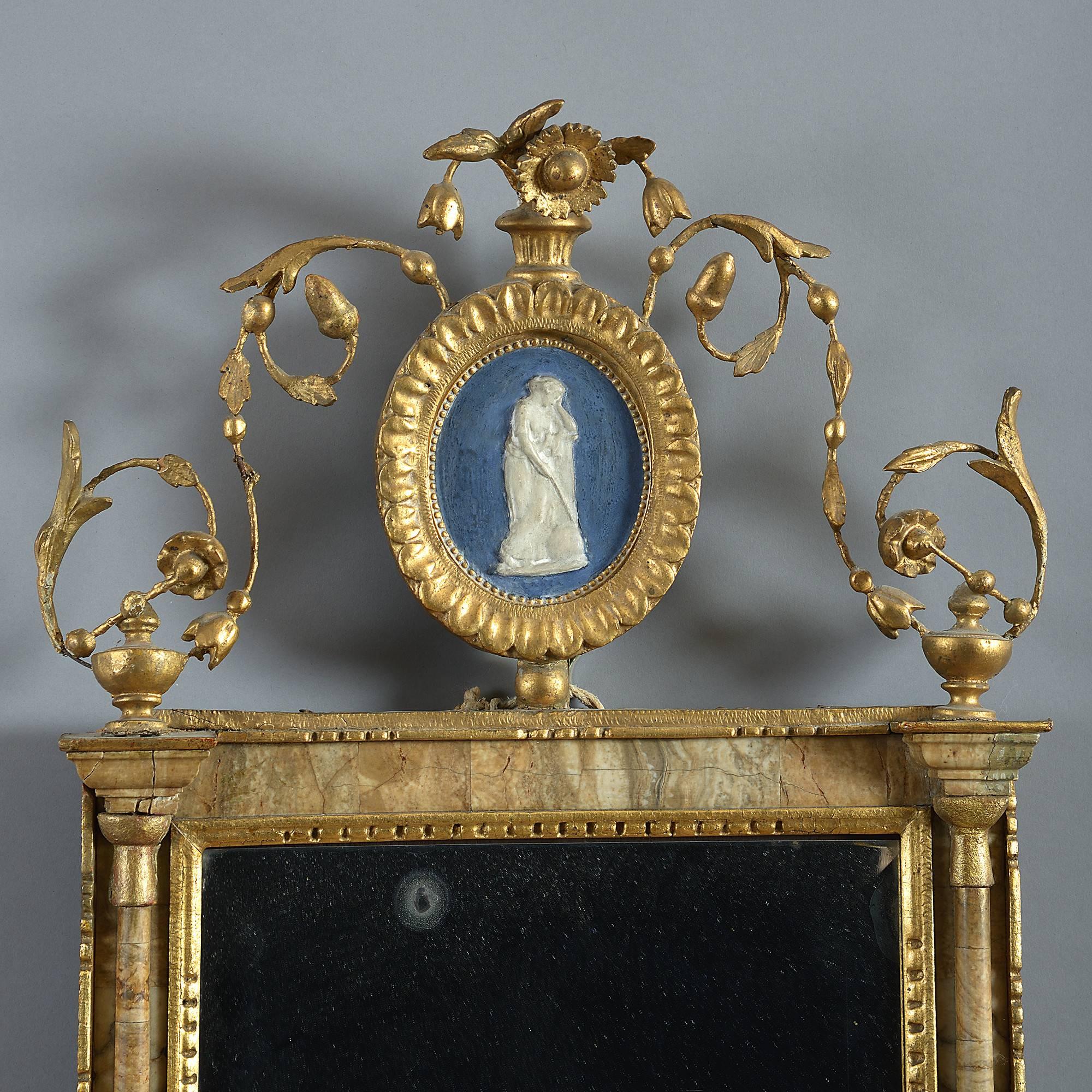 A late 18th century giltwood mirror in the Classical taste, the scrolling crest with painted plaque, supported upon alabaster columns and housing an old beveled plate.