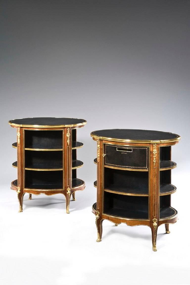 A pair of open library bookcases are inset with oval black leather tops within moulded surrounds above three-tiered shelves. The shelves are divided to the angles by fluted pilasters headed by ribbon-tied garlands. The bookcases stand on cabriole