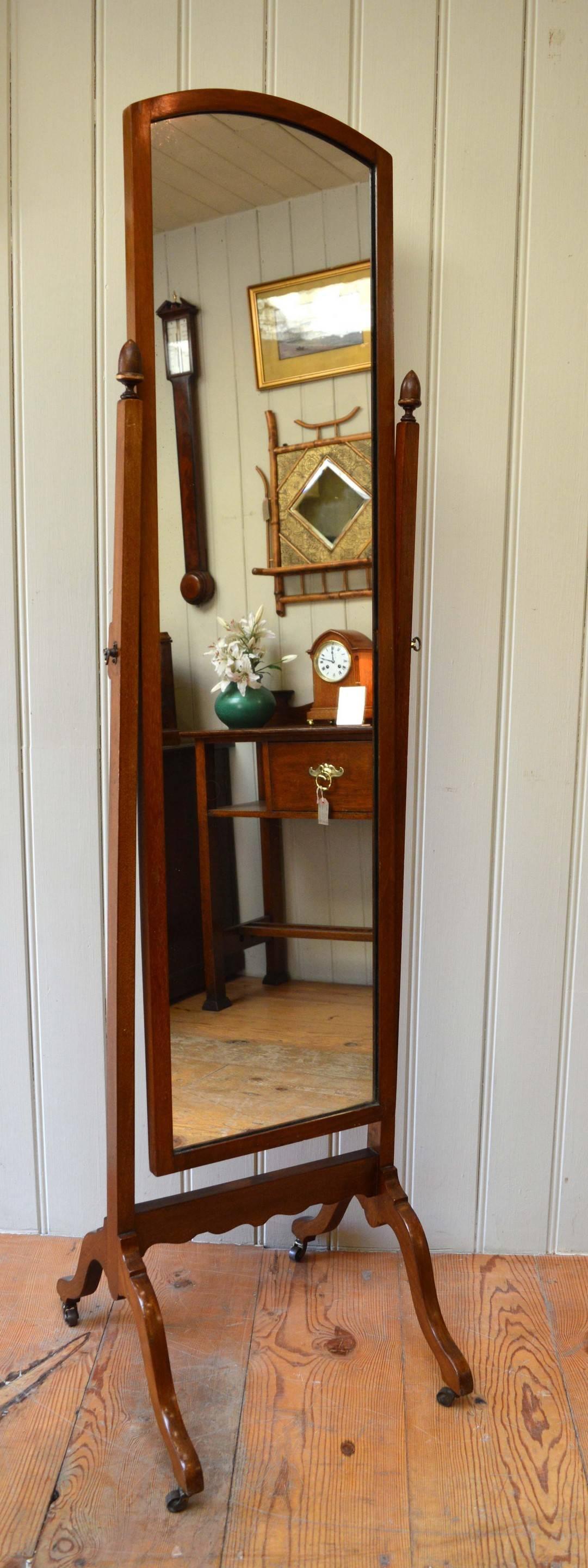 1920s mahogany cheval mirror with wooden finials and raised on outsplayed supports with brass castors.