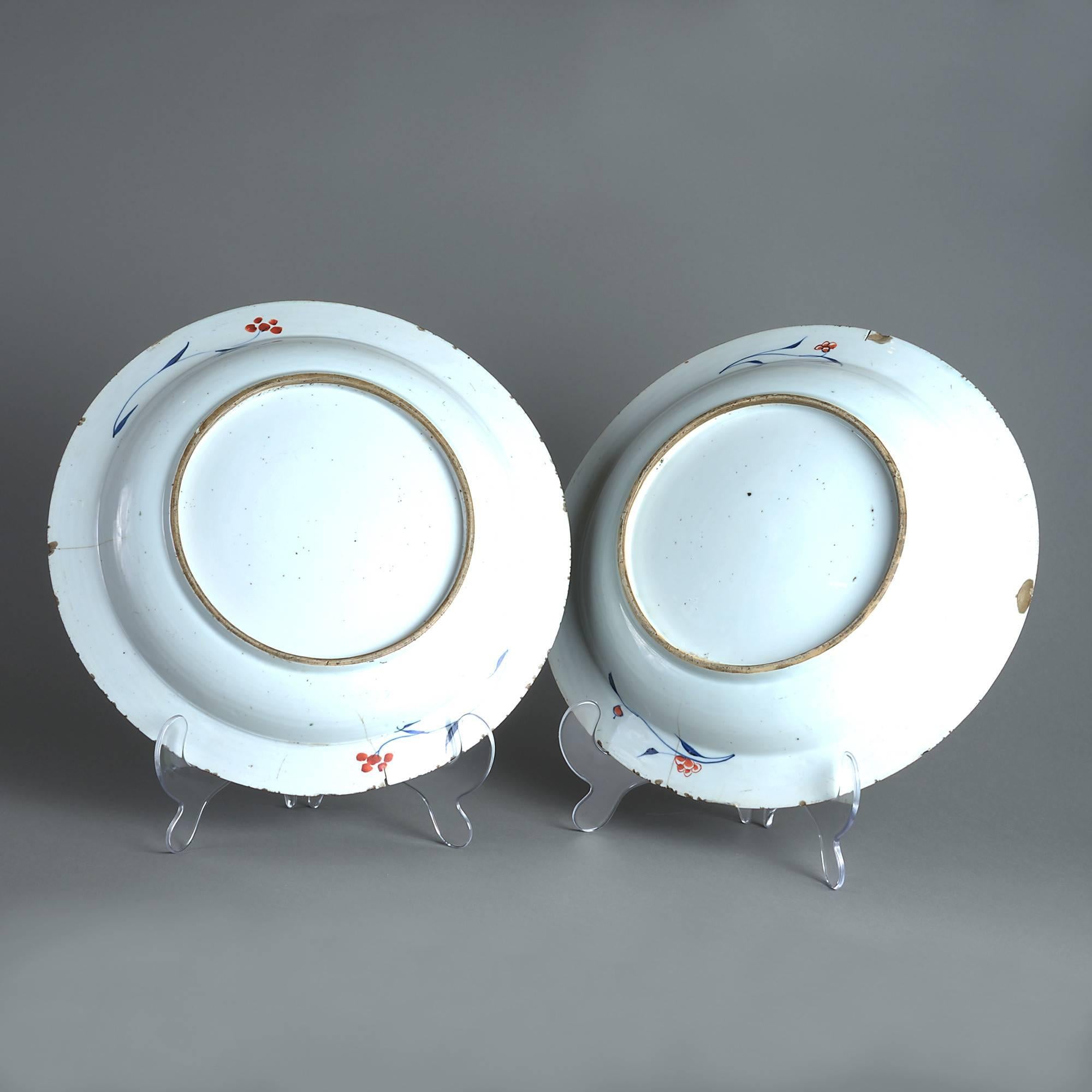 A pair of early 18th century porcelain chargers, decorated with stylized flowers and foliage in polychrome glazes upon a white ground in imitation of Japanese Imari. 

Condition: Commensurate with age (minor hairlines and fritting to underside).