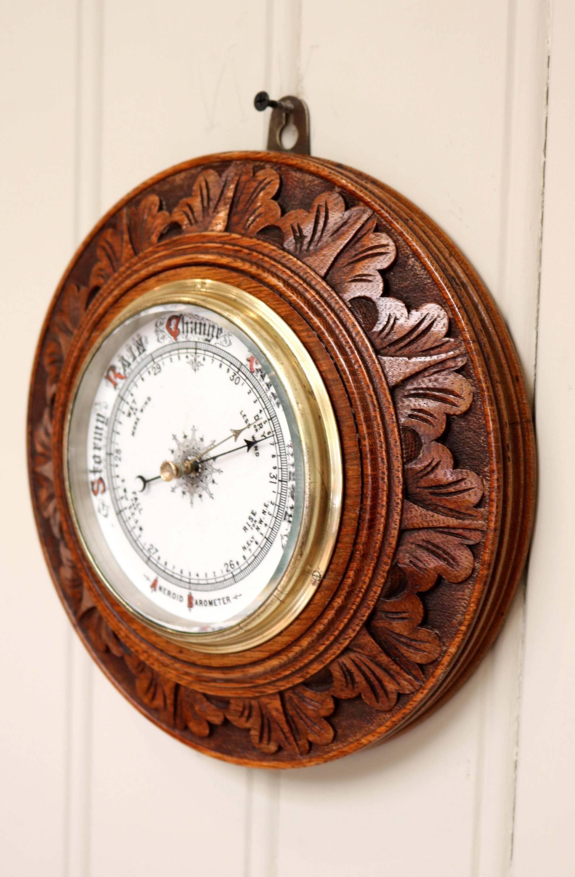 Edwardian carved oak circular barometer having a ceramic dial with hand-painted scale and lettering with an aneroid movement.