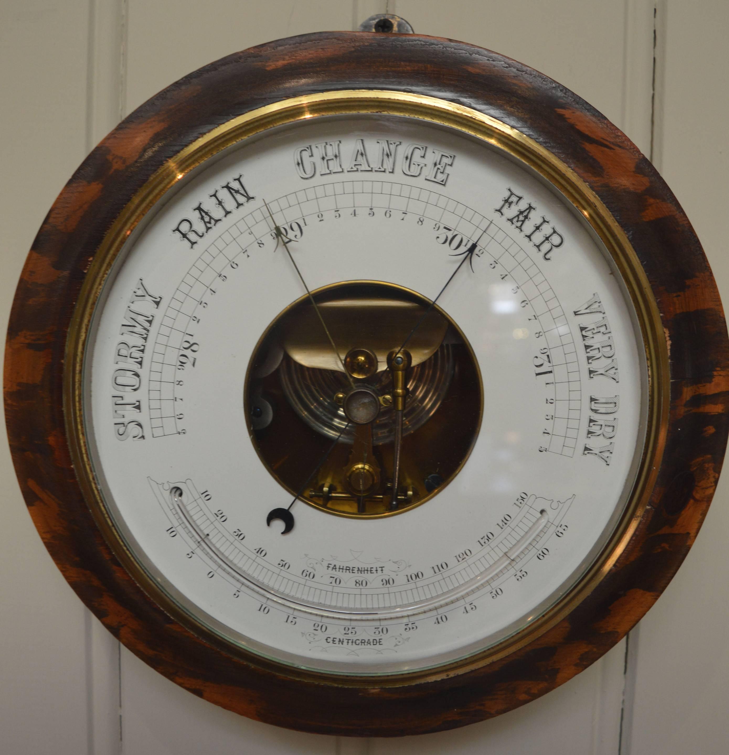 A large grained fruitwood aneroid barometer. It has a heavy solid fruitwood case, with a stepped edge and a grained finish. The brass bezel has a thick bevel edge glass, behind which is a white dial showing the atmospheric pressure and a curved