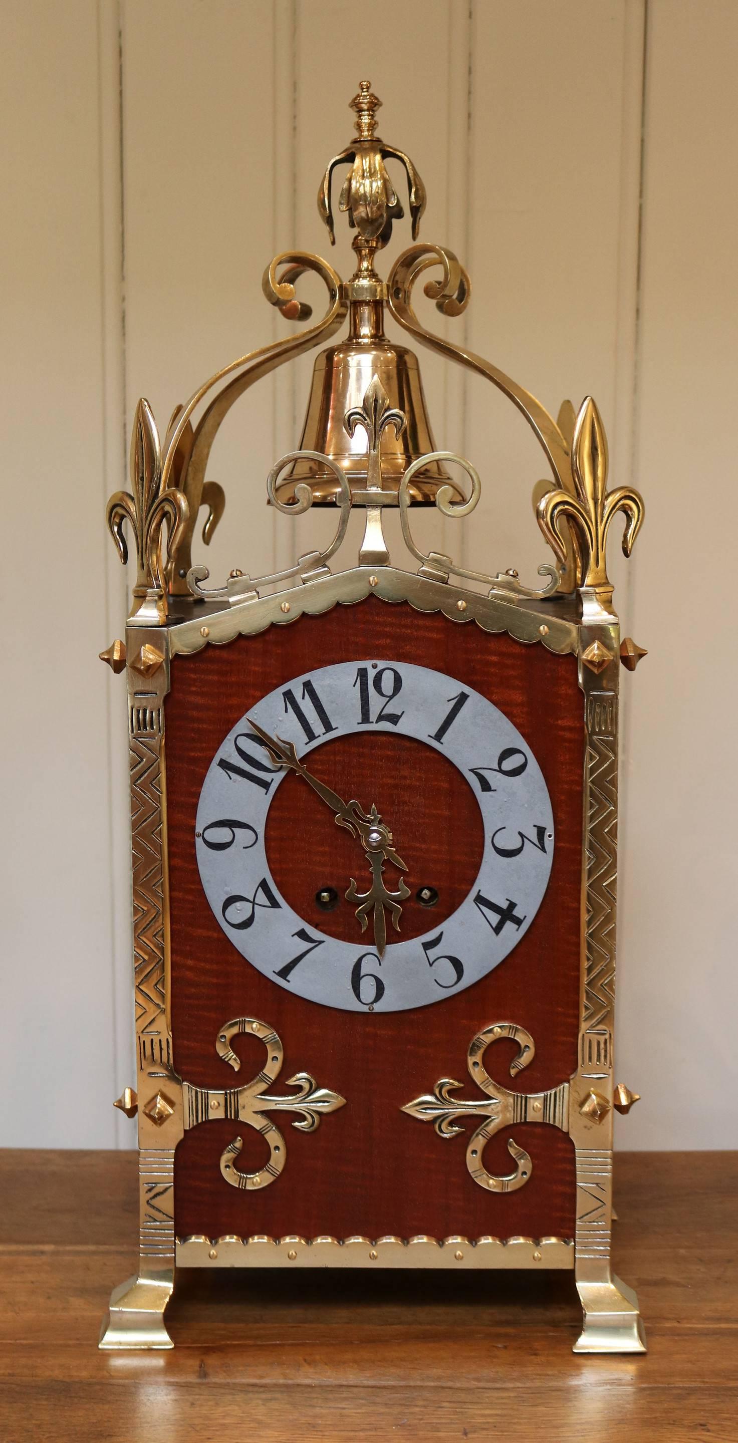 A very impressive mahogany and brass Gothic style clock garniture, dating to the early 1900s. The clock has a solid rectangular case, veneered in fiddle back mahogany, with a stylized silvered chapter ring. The brass frame has fleur de lis terminals