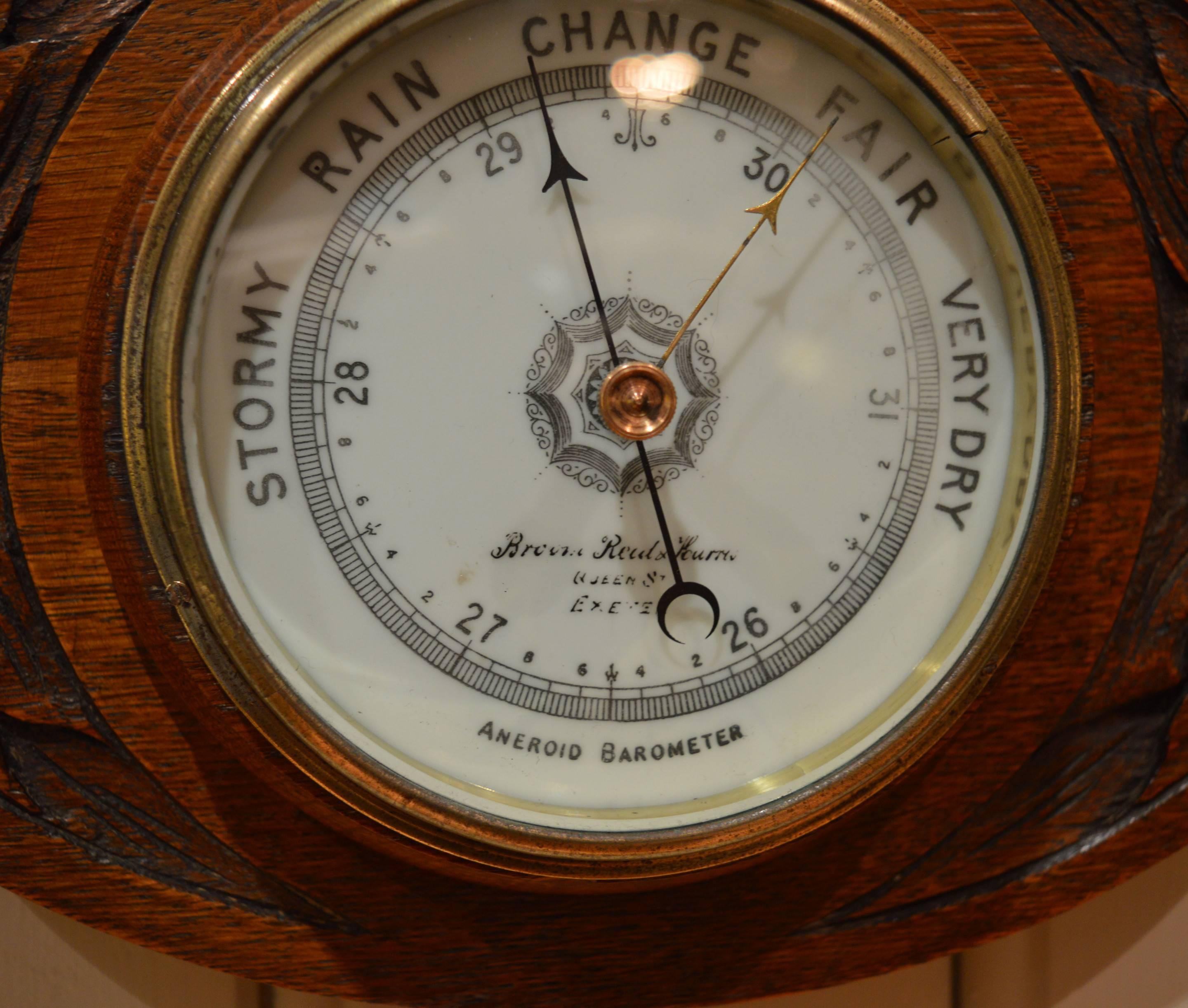 An early 20th century solid oak aneroid wall barometer. It has a carved case, brass bezel and a bevel edge glass. The milk glass dial is signed by the original retailers, brown, read and Harris of Queen Street, Exeter.